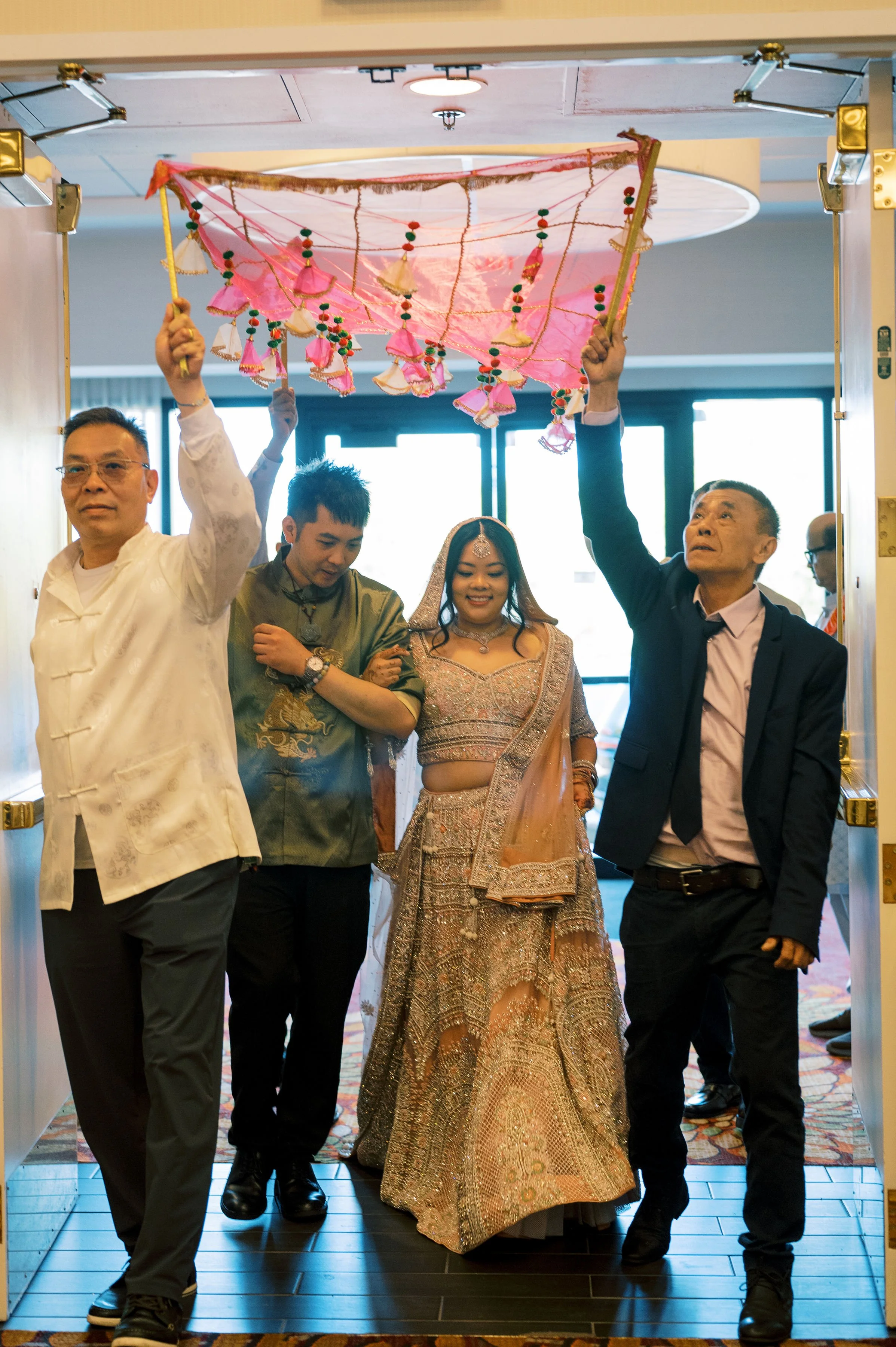 People carrying a decorative pink parasol with tassels at a celebration or event, walking through an entrance.