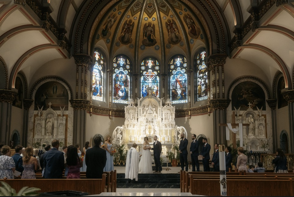 A wedding ceremony inside a church with a decorative altar, stained glass windows, and a congregation.