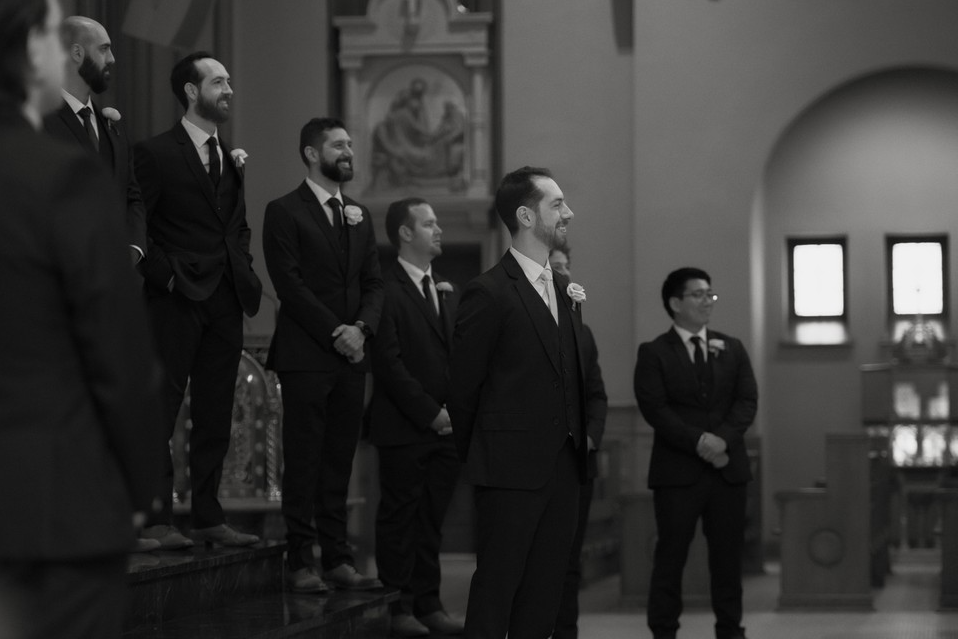 Group of men in suits standing in a church, some smiling.