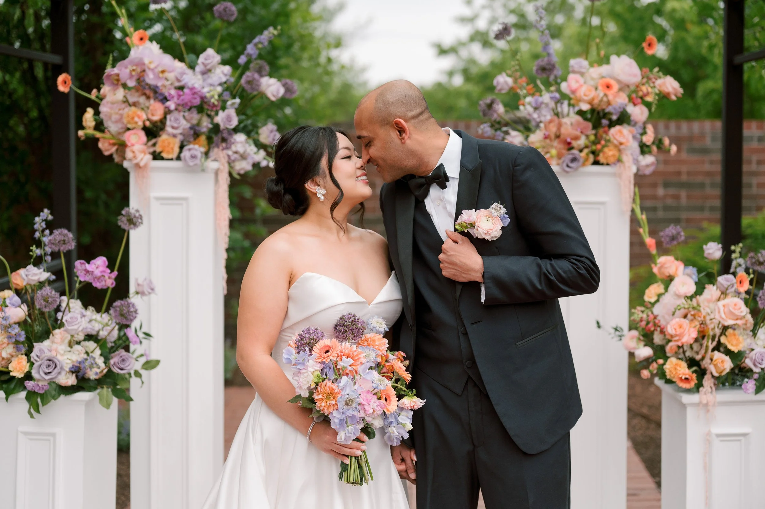 A bride and groom sharing a moment at their wedding, surrounded by colorful flowers and floral arrangements.