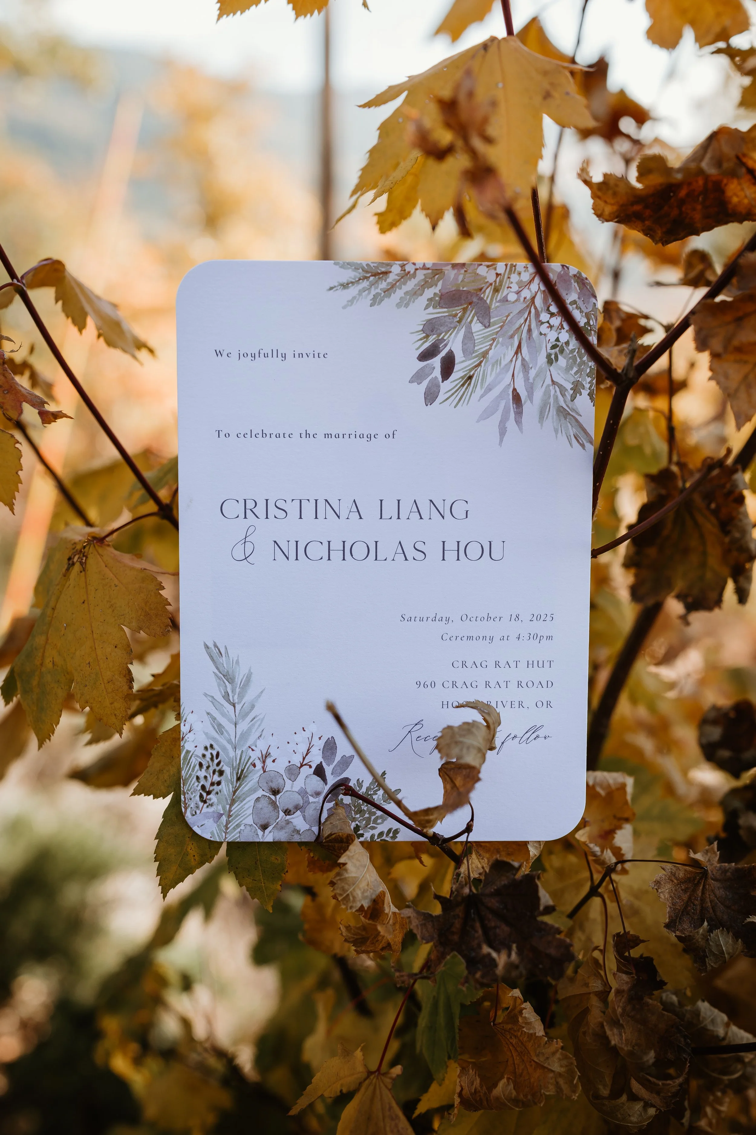 A wedding invitation card hanging on autumn leaves.