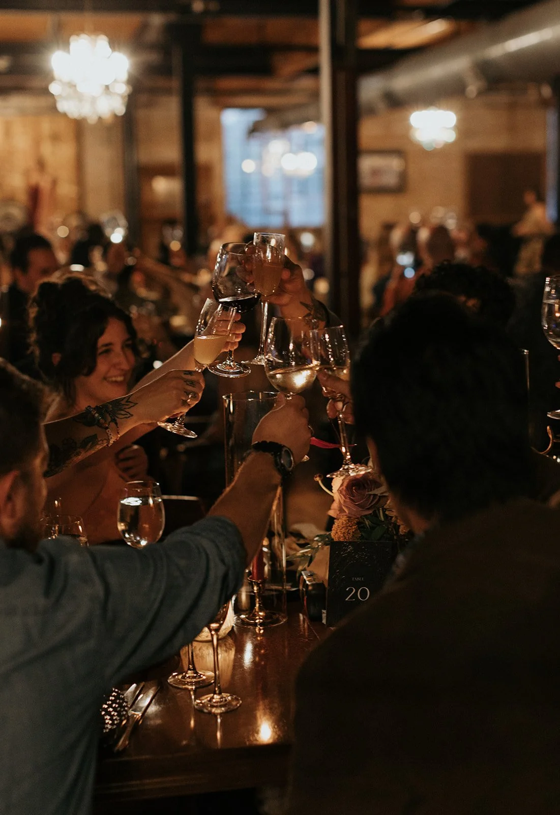 People at a dimly lit restaurant or bar raising glasses in a toast, celebrating with wine and cocktails.