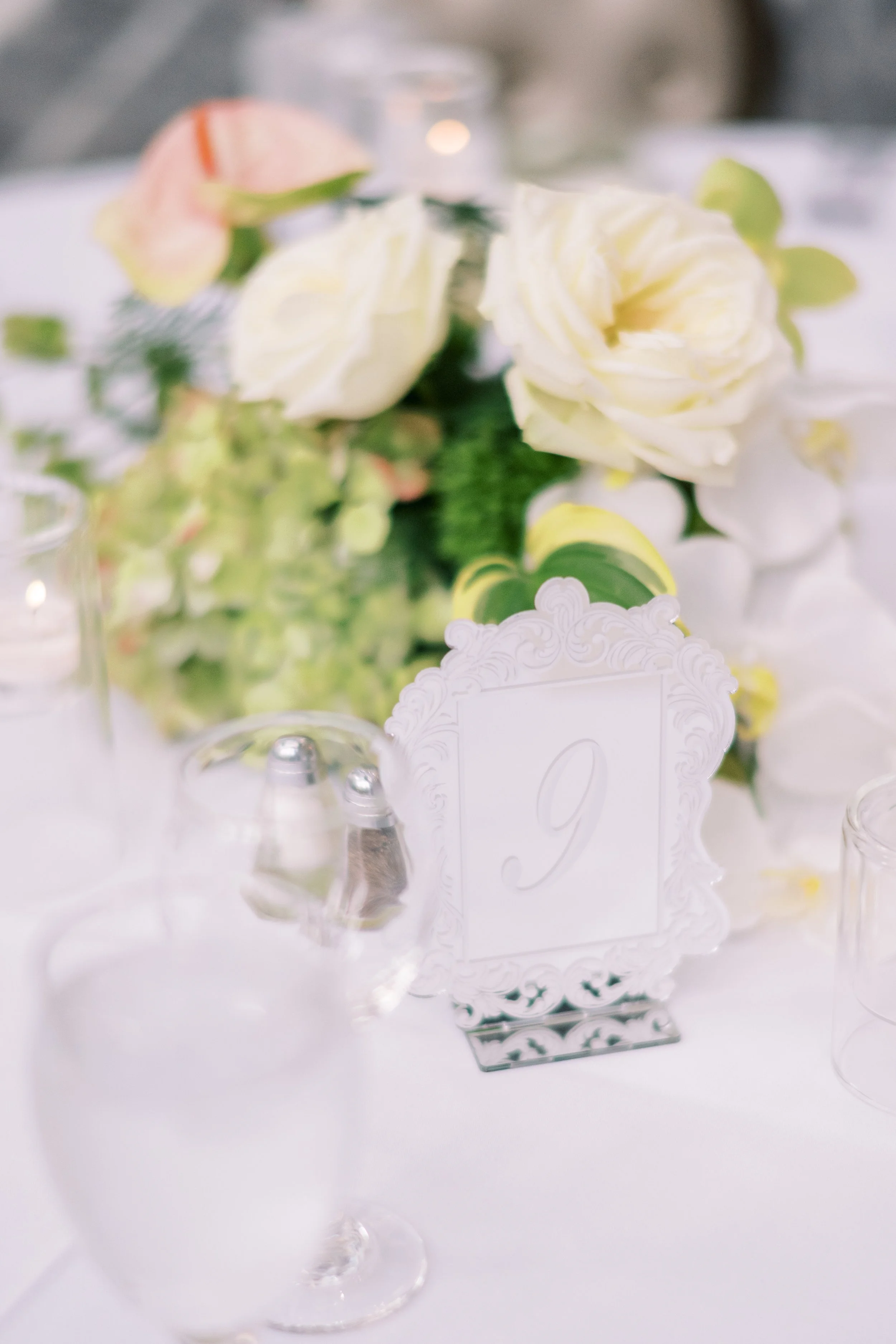 Close-up of a flower arrangement with white roses and pink-tipped flowers on a white table, with a decorative frame and salt and pepper shakers in the foreground.