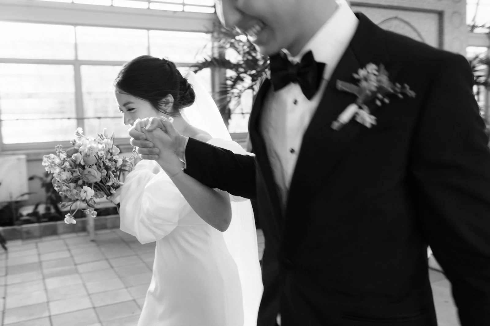 Black and white photo of a bride and groom holding hands and walking.