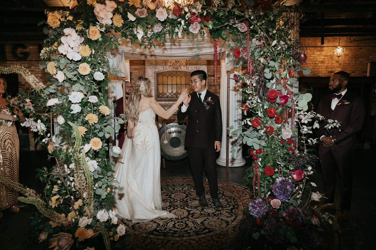 A wedding ceremony with a bride and groom exchanging high-fives, surrounded by floral decorations and guests in formal attire.