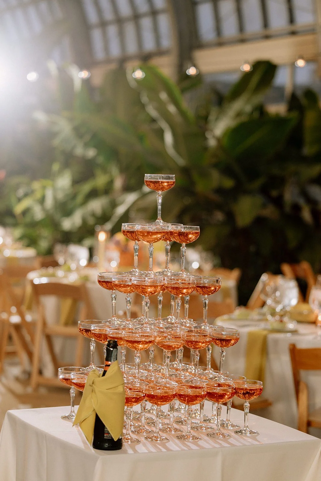 A pyramid of champagne glasses filled with rosé champagne on a white table at an event or celebration.