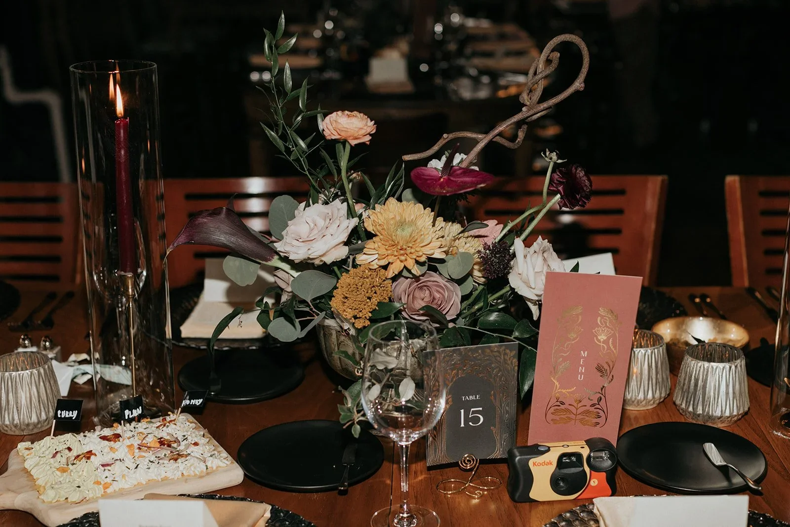 A table centerpiece with a large bouquet of flowers, candles, and event decor, set for a formal dinner with table number 15.