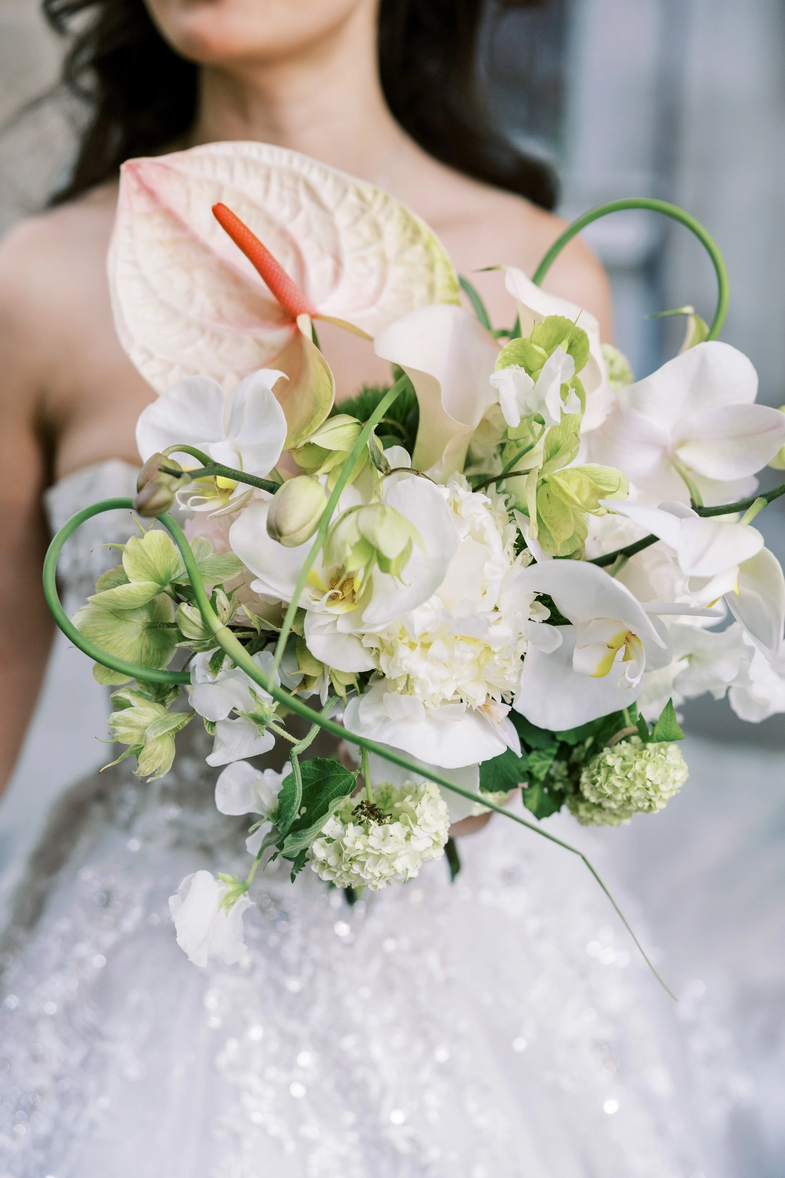 Close-up of a woman in a wedding dress holding a bouquet of white and green flowers, including an anthurium with a red spadix.