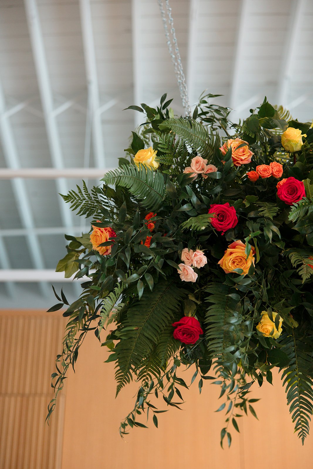 A hanging floral arrangement with colorful roses and green foliage, set against a blurred indoor background.