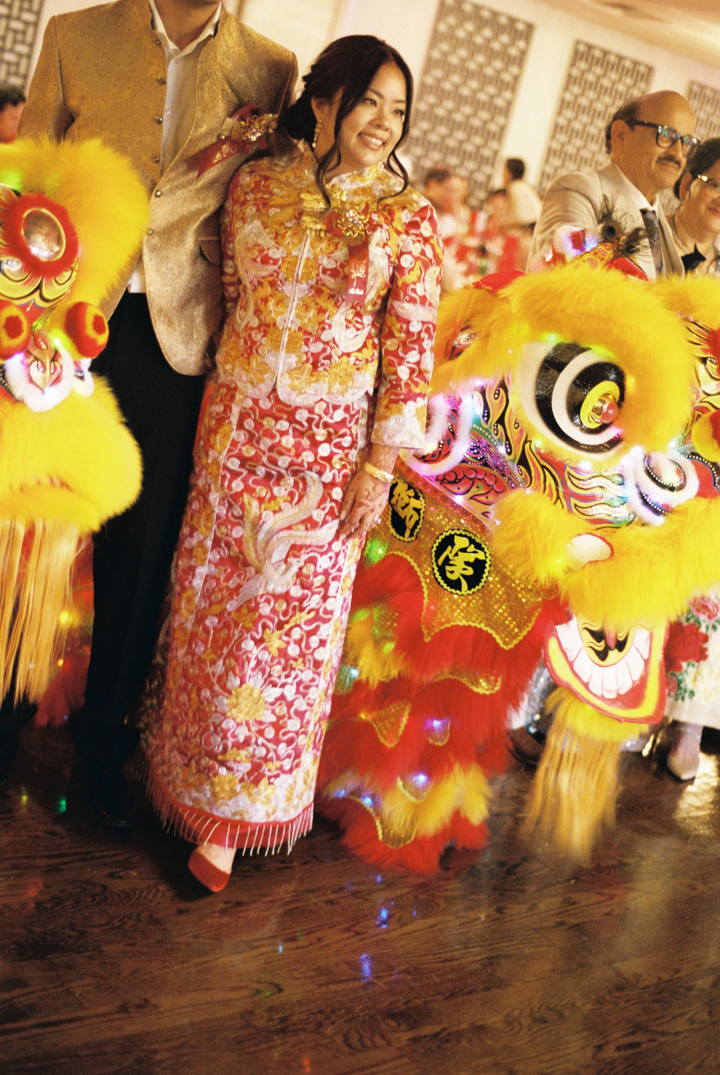 People dressed in traditional Chinese costumes participating in a cultural celebration, with a colorful lion dance attire in a festive indoor setting.
