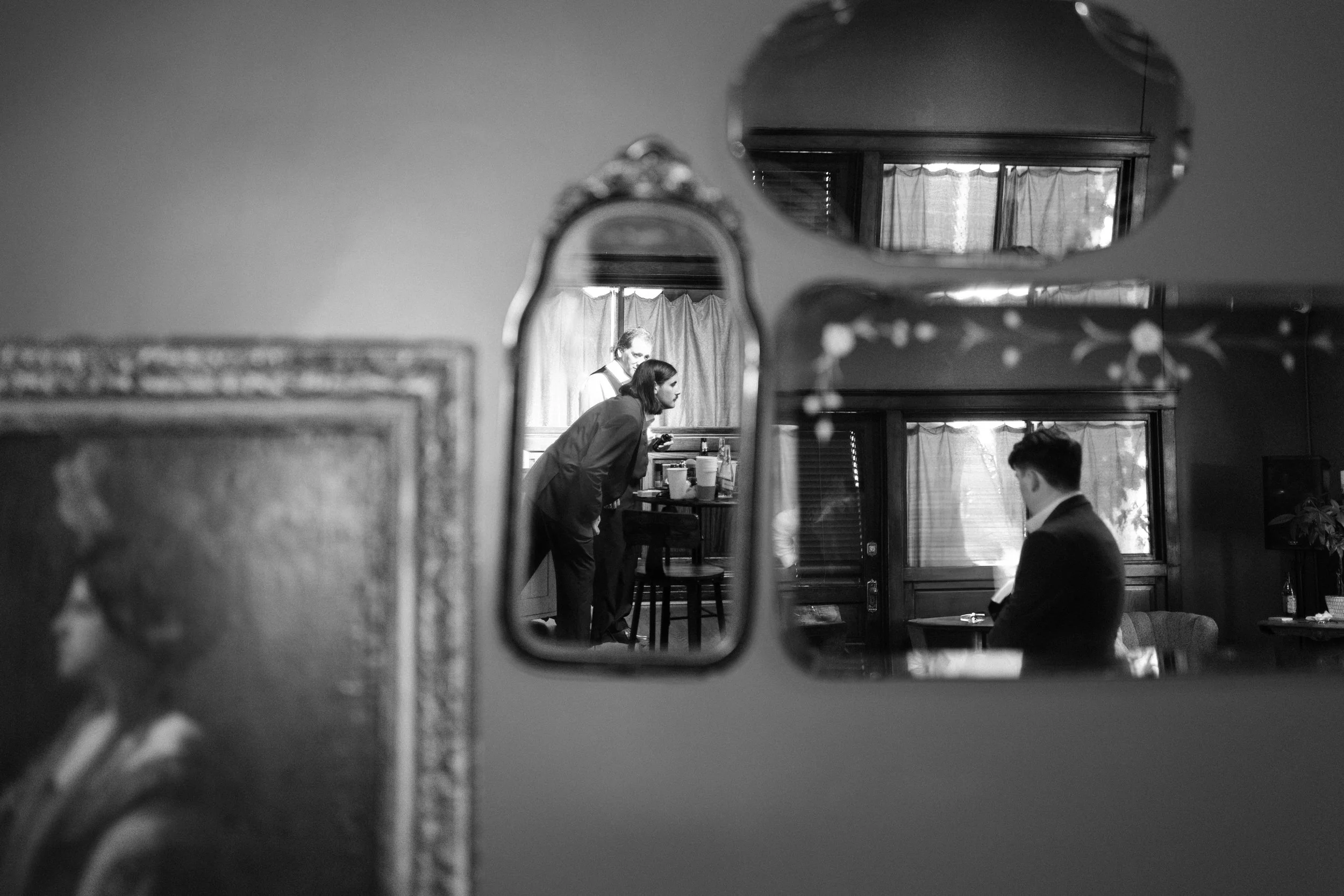 Reflection of a man and woman through a mirror in a warmly lit room with curtains, showing two people in conversation or interaction.