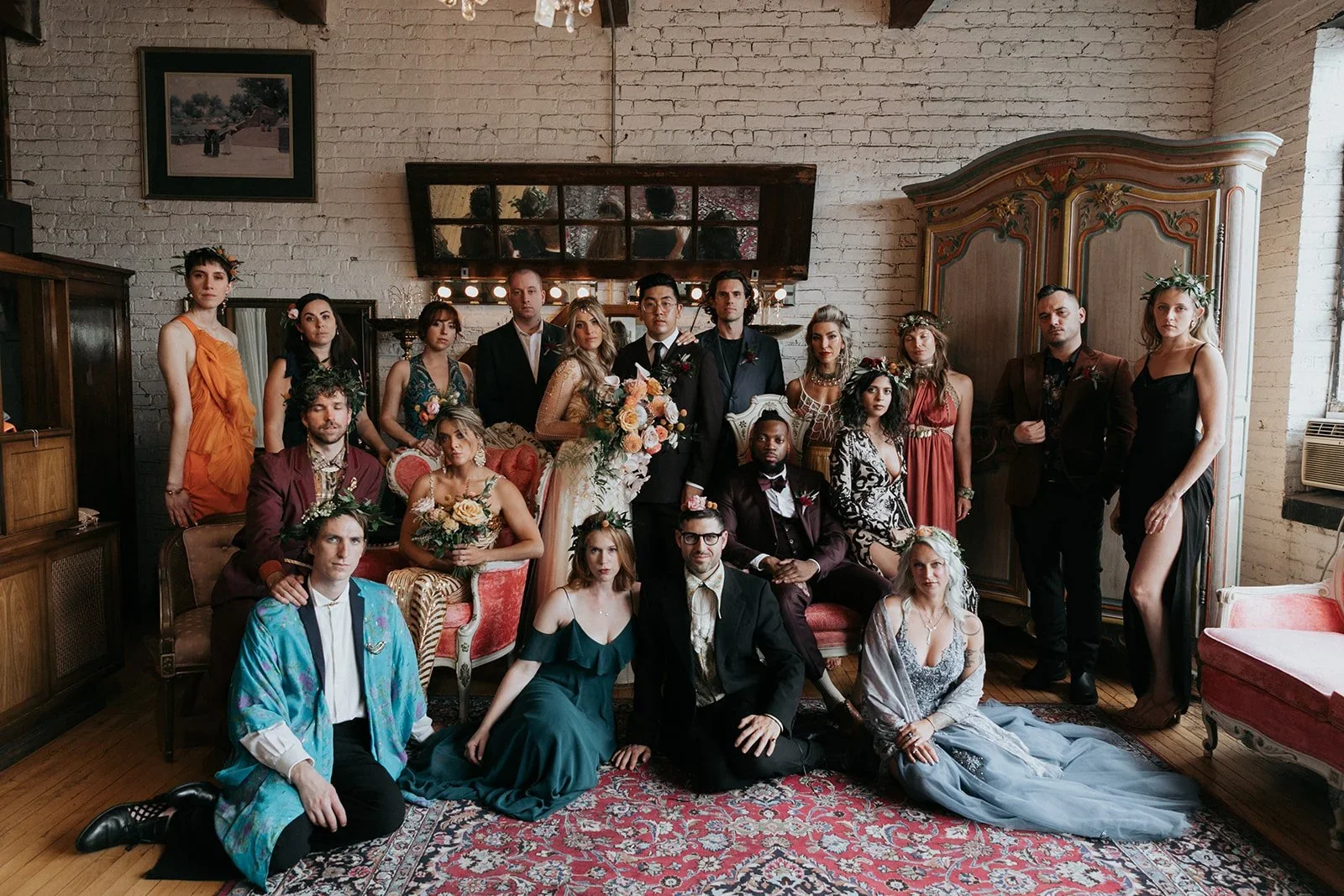 A diverse group of people gathered in a room with vintage furniture and exposed brick walls for a formal event, possibly a wedding or celebration.
