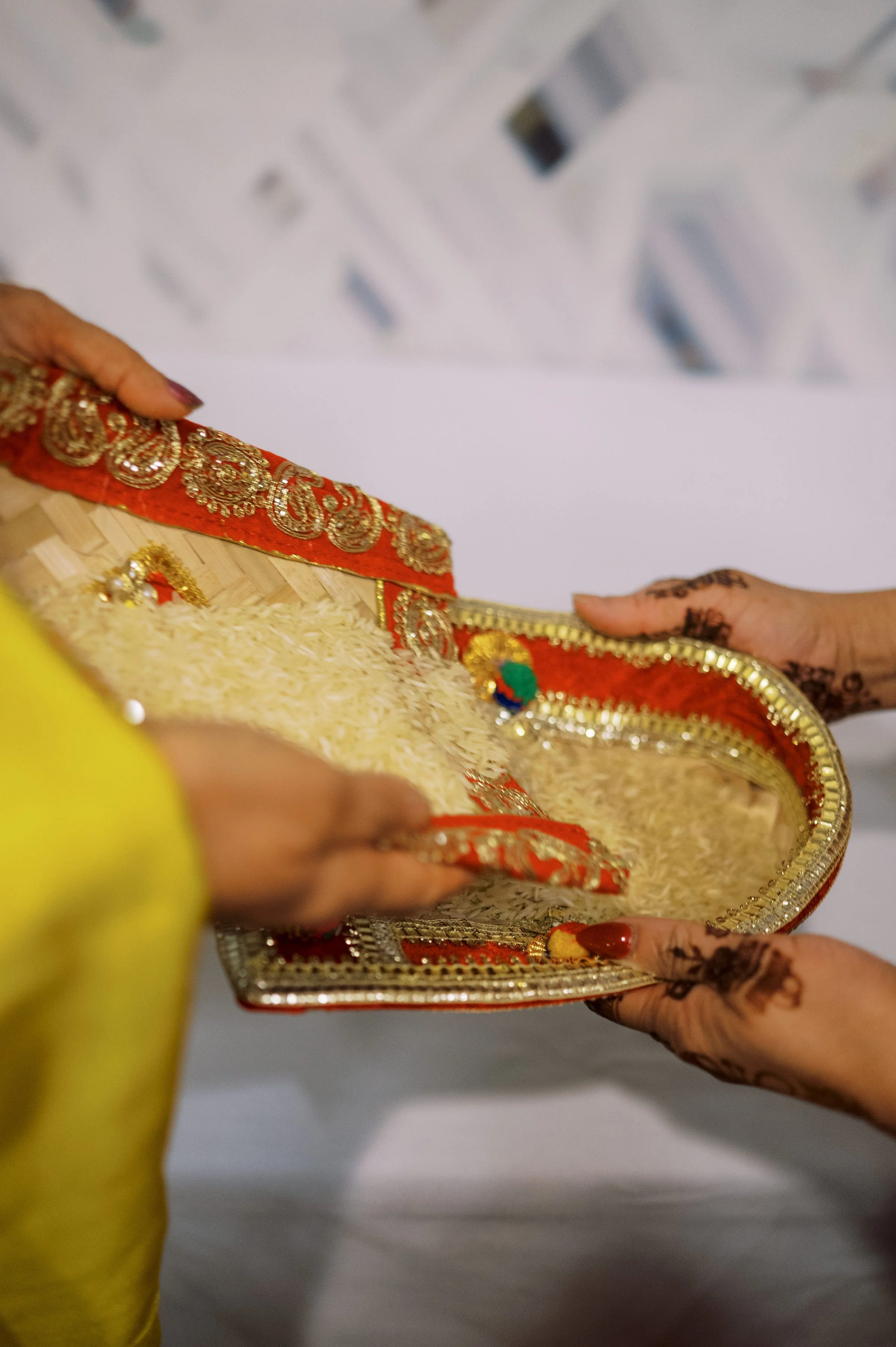 Close-up of hands holding a decorated tray, with henna designs on fingers, during an Indian celebration or ceremony.