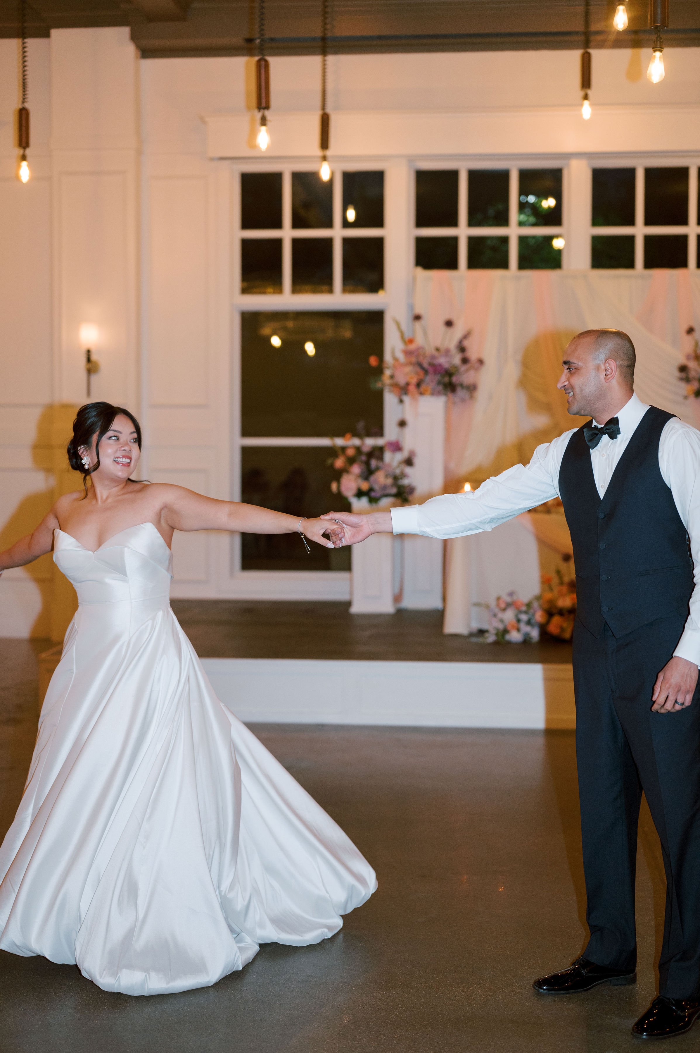 A bride and groom dancing at their wedding reception, holding hands and smiling.