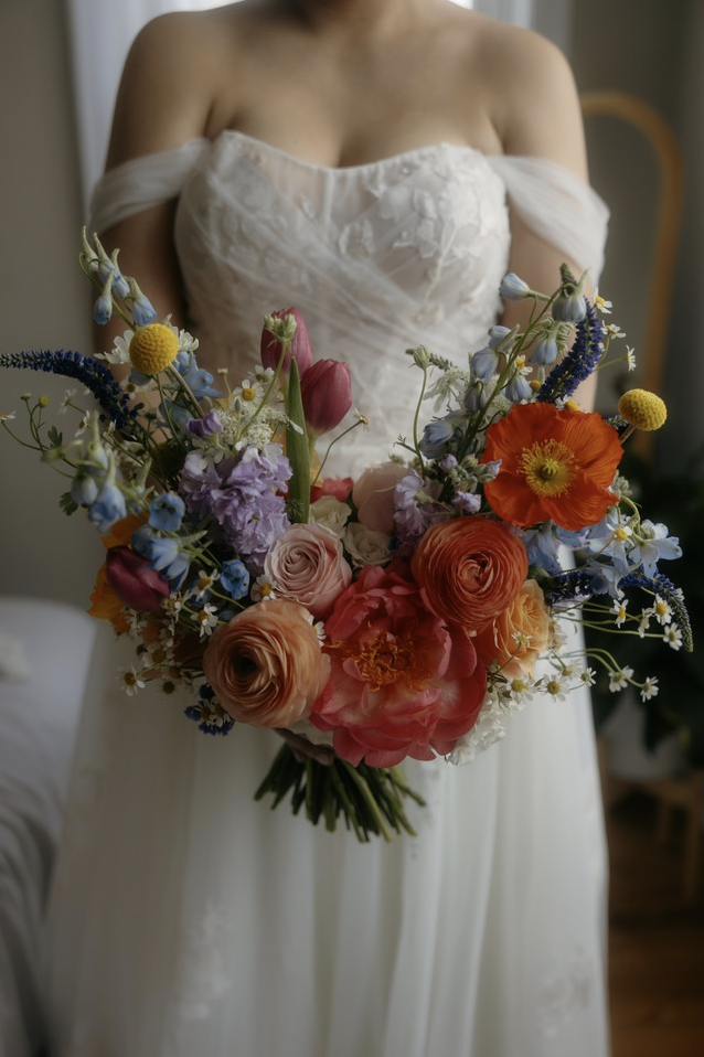 Bride in a white wedding dress holding a large colorful bouquet of flowers including roses, tulips, and other blooms.