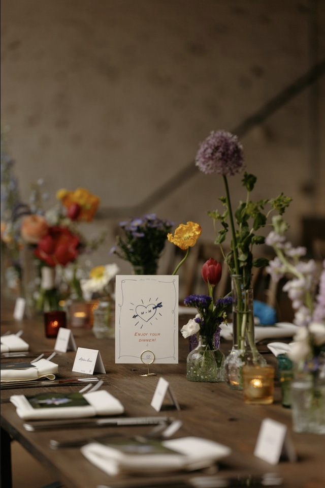 A decorated dining table with floral centerpieces, candles, and place cards, featuring a sign that says "Enjoy Your Dinner!" in a vintage-style setting.
