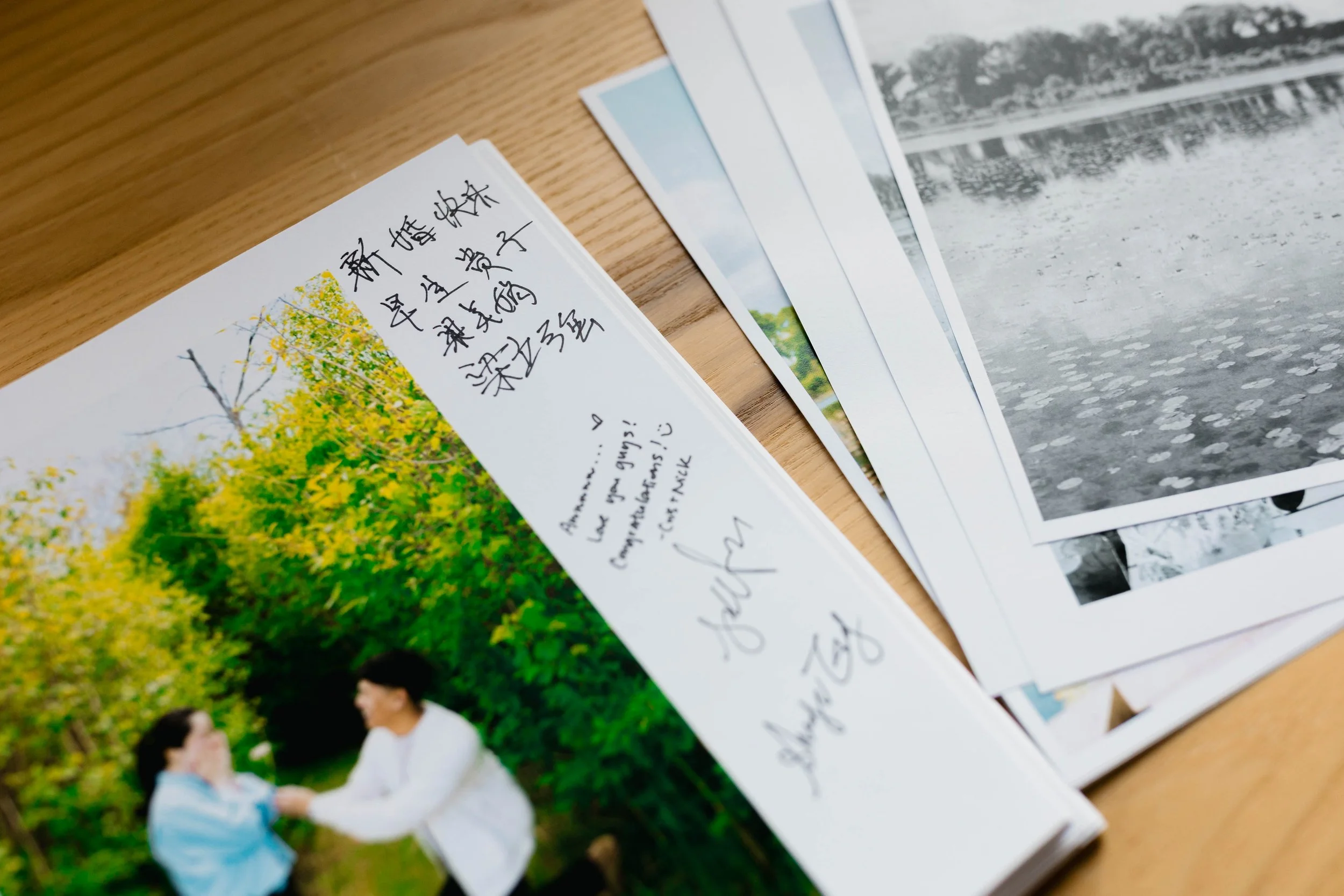 Close-up of a handwritten postcard with Chinese characters and a colorful printed image of yellow flowers. Several other postcards with images are partially visible, spread out on a wooden surface.