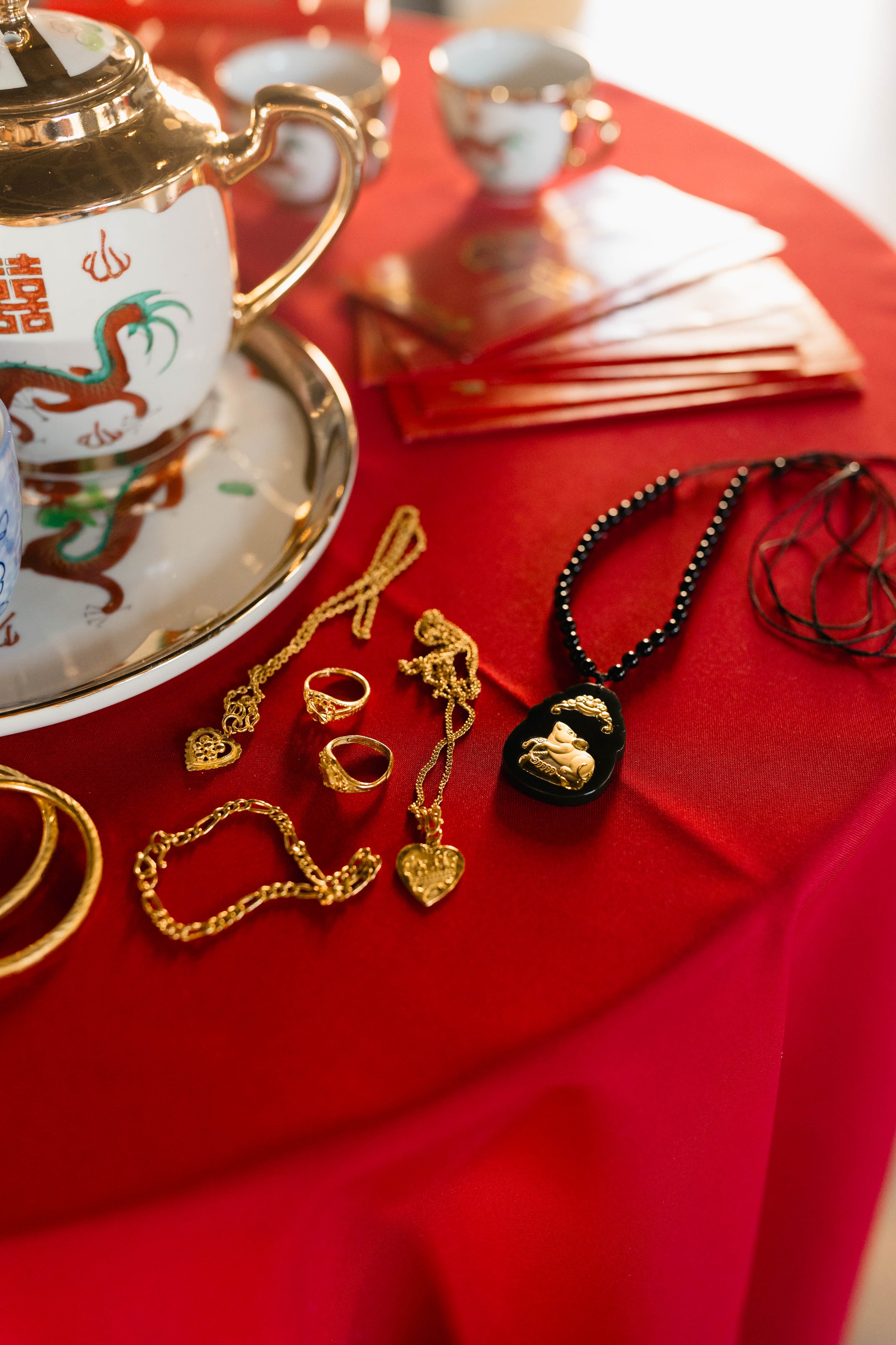 Jewelry collection on a red tablecloth with a gold and white teapot, teacups, and assorted necklaces, rings, and bracelets.