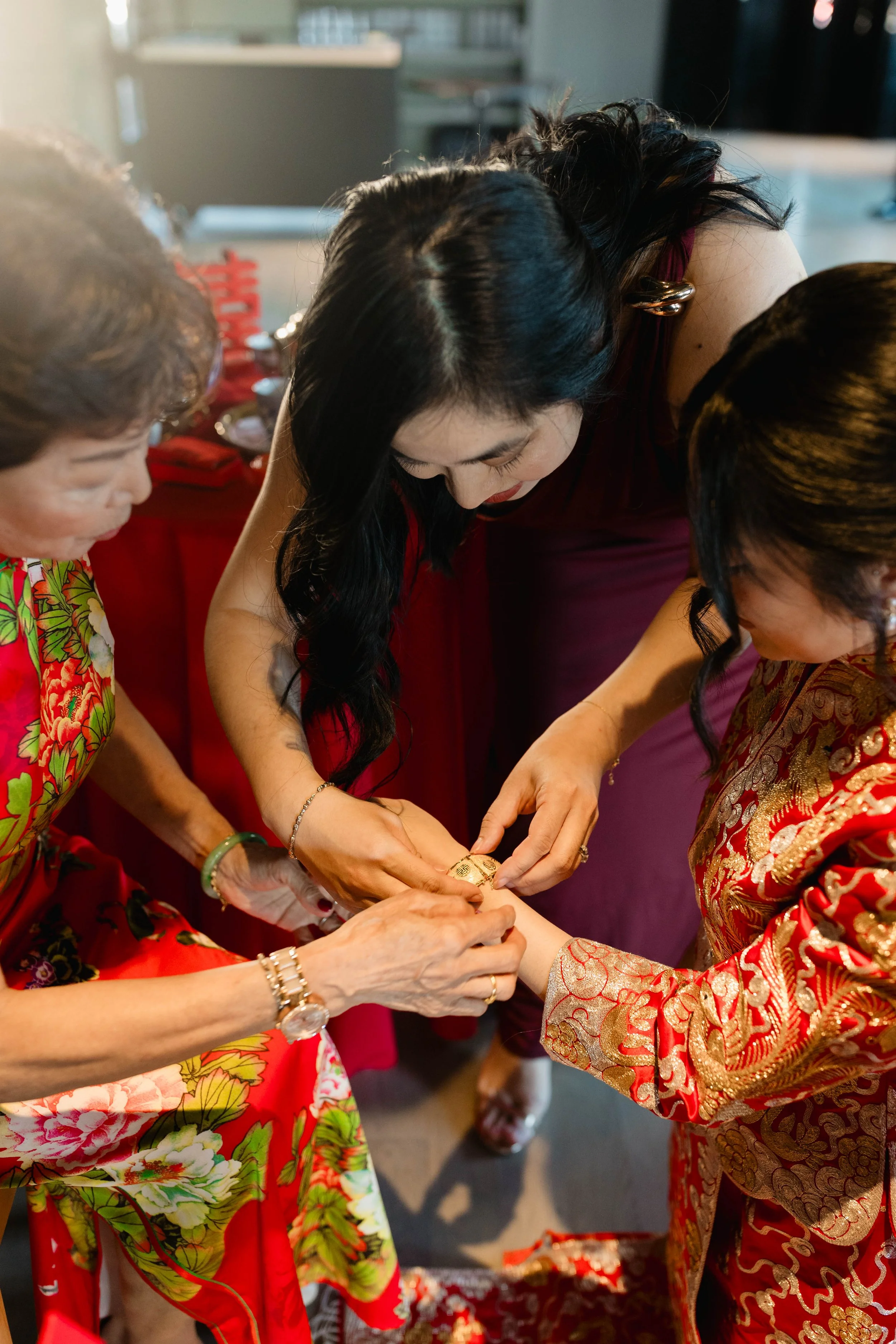 Women involved in a traditional wedding ceremony, with one woman in a vibrant red and gold embroidered dress and another in a floral dress, exchanging rings or jewelry.