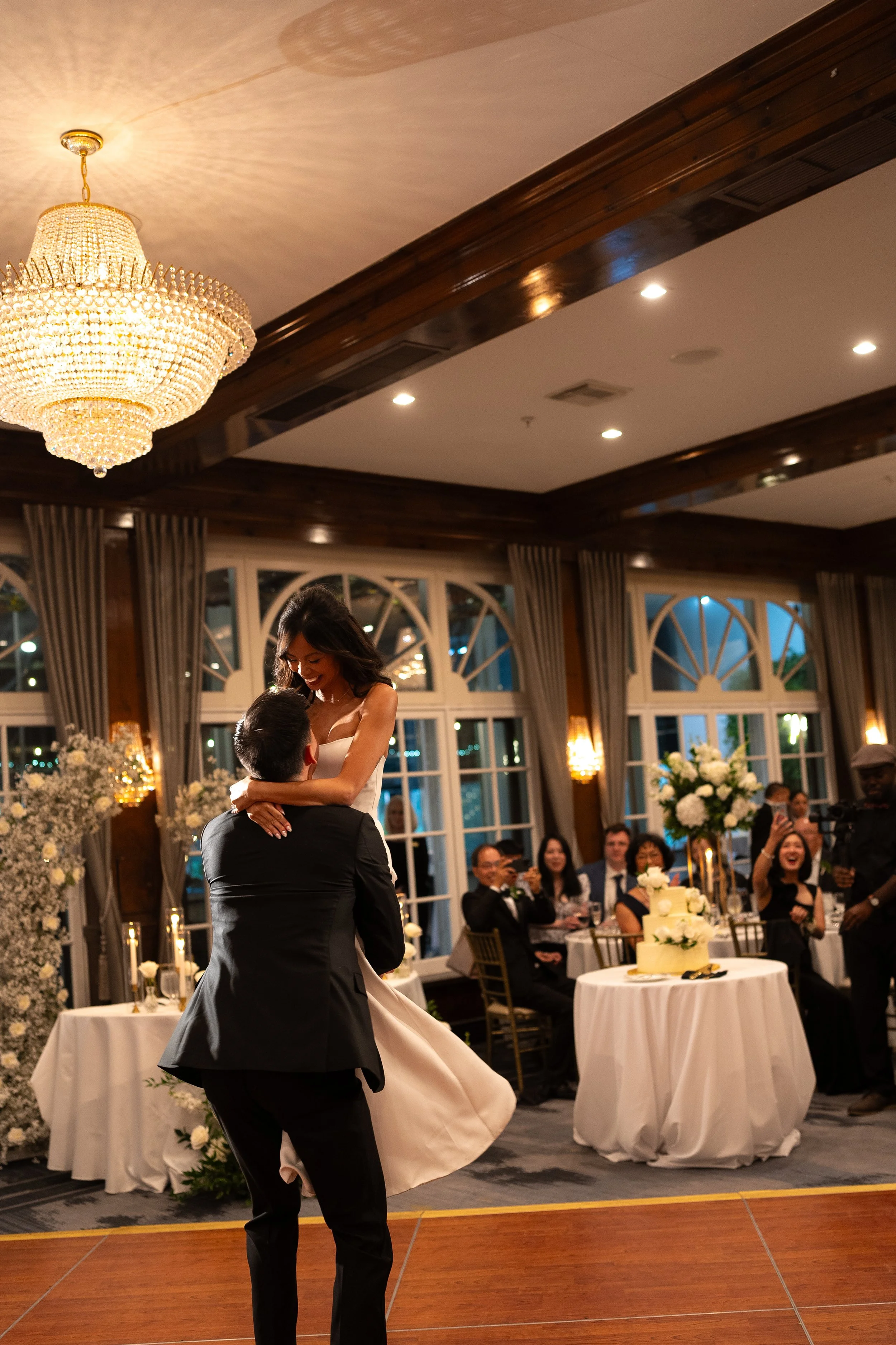 A bride and groom sharing a dance at their wedding reception, with guests seated at decorated tables in the background.