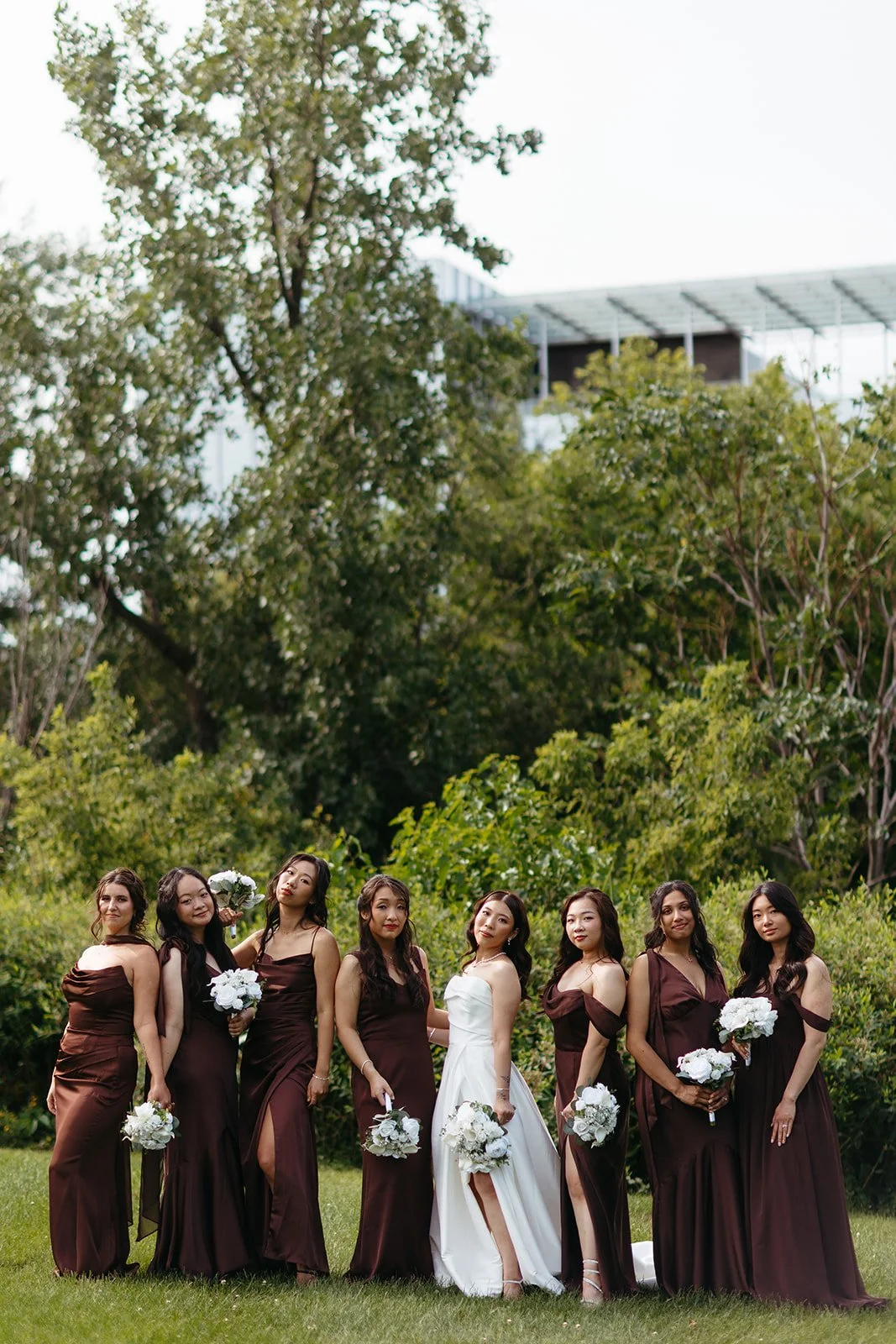 Bridesmaid taking photos with the bride wearing brown dresses with bouquets in hand during the wedding day