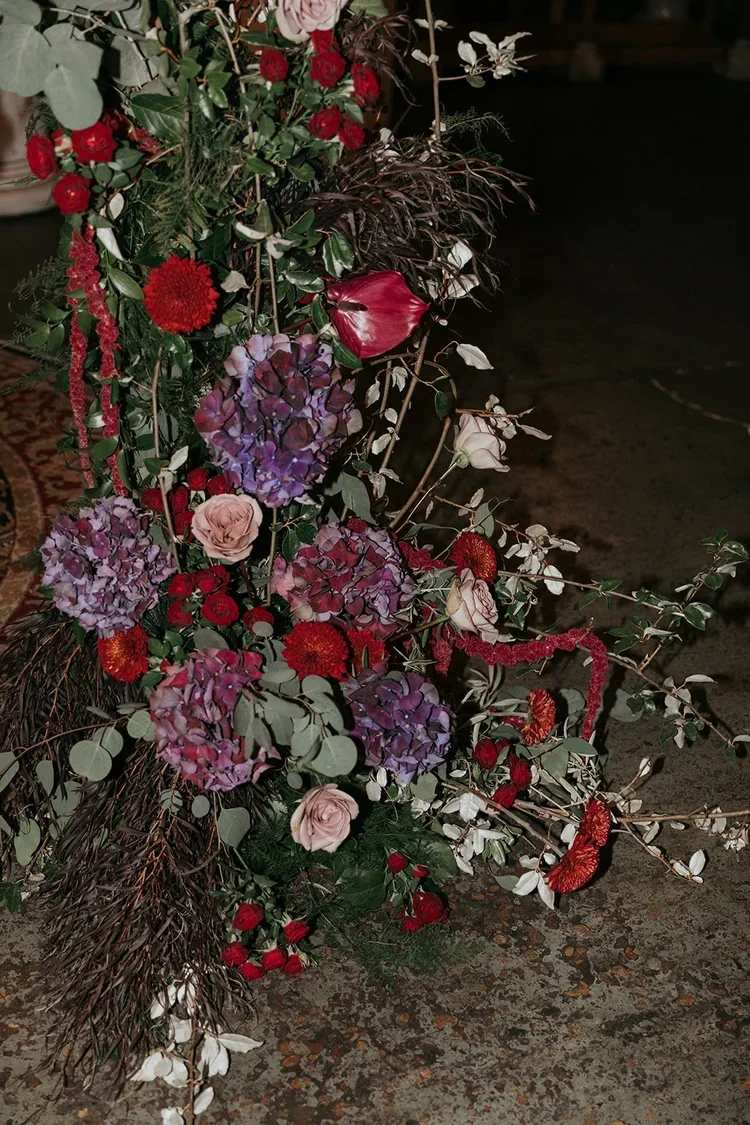 Elegant floral arrangement with purple hydrangeas, red roses, pink roses, and various greenery.