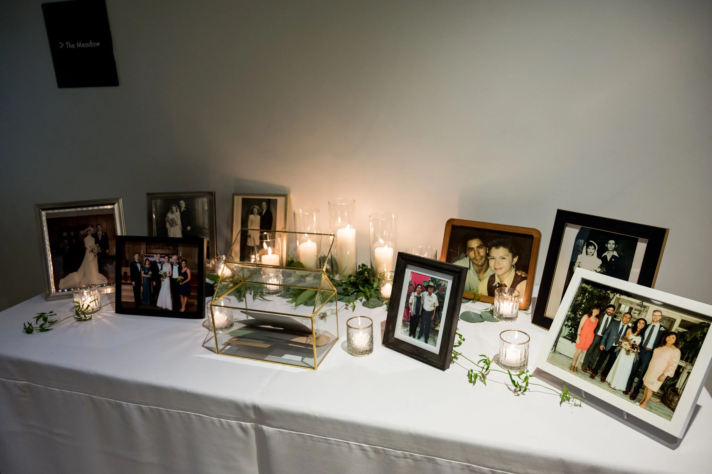 Table displaying various framed family and wedding photos decorated with candles and greenery.