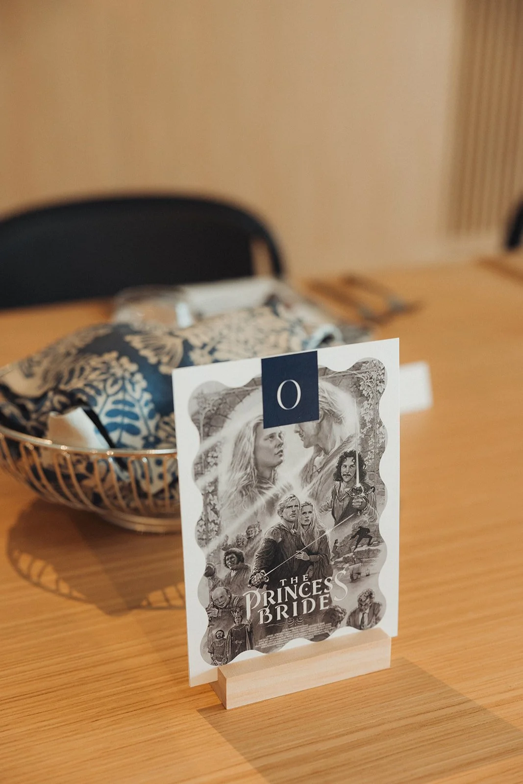Table card featuring artwork from the movie 'The Princess Bride' on a wooden table, with a basket of fabric and blurred background.