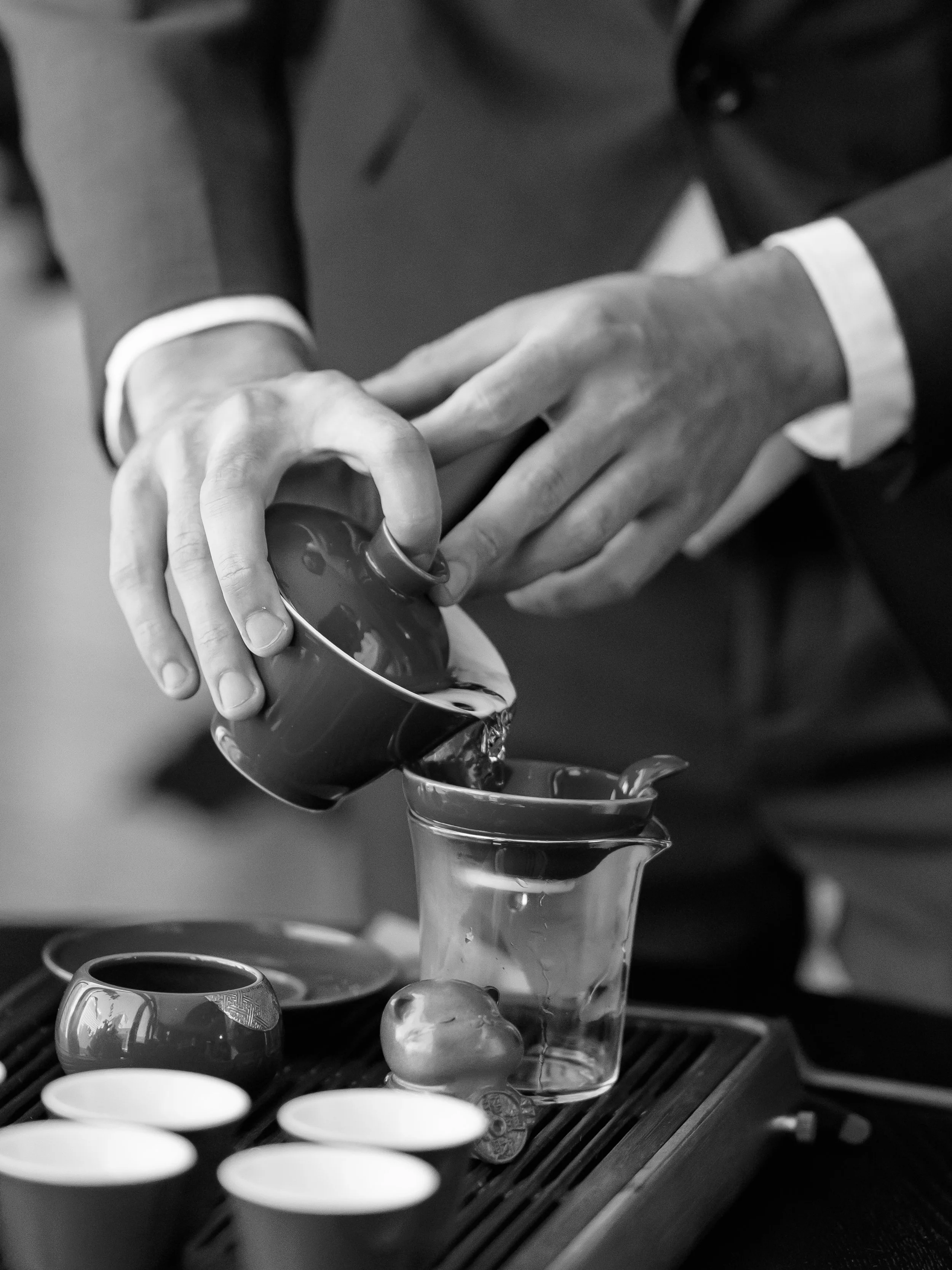 People serving hot beverages, possibly tea or coffee, into small cups.