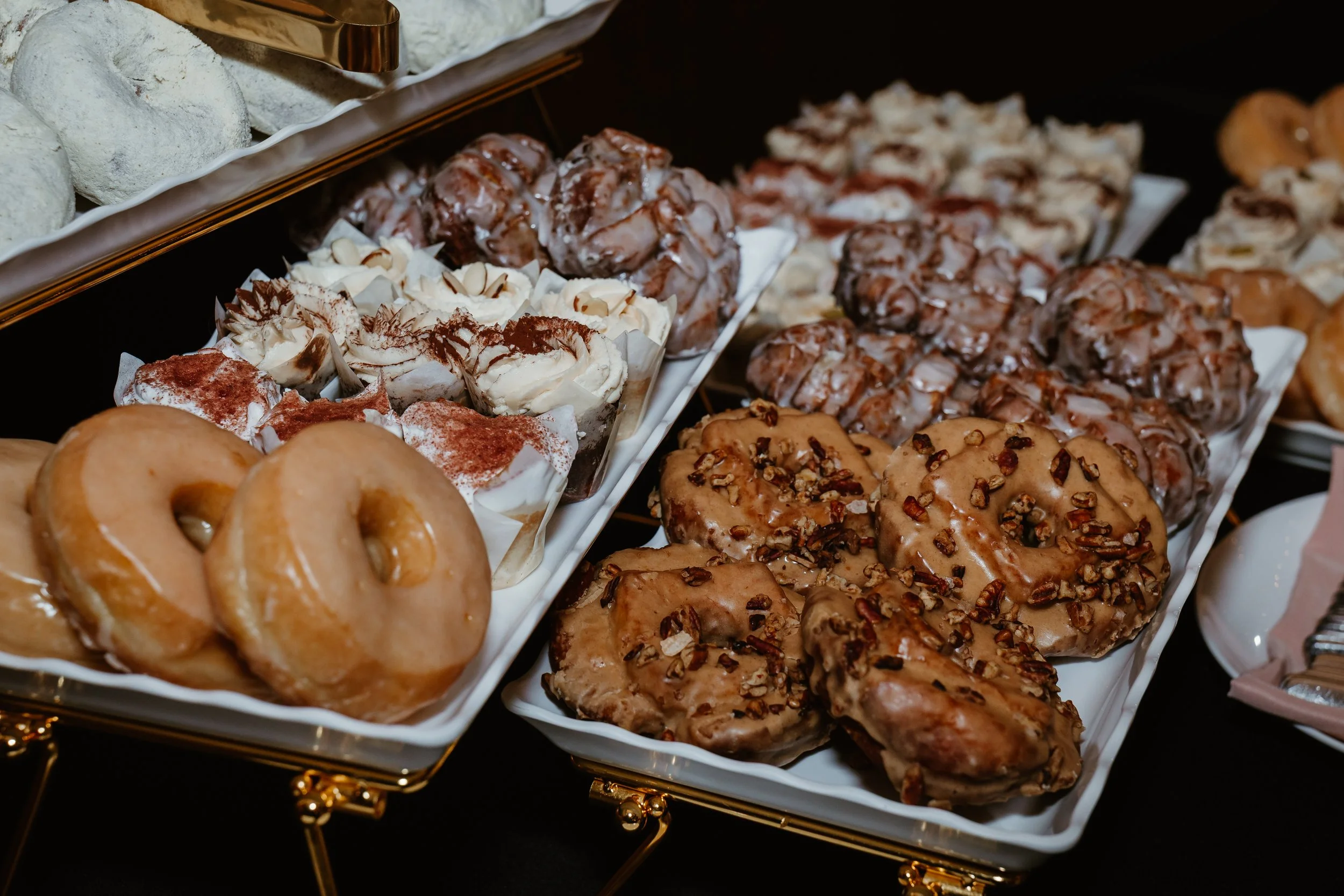 Assorted pastries including donuts, topped with various glazes, nuts, and whipped toppings, on a serving tray.