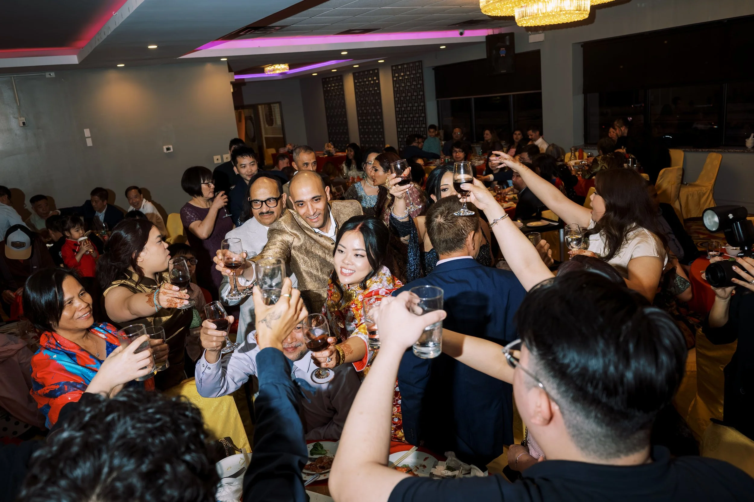 People gathered at a celebration or dinner party, raising their glasses in a toast inside a decorated banquet hall.