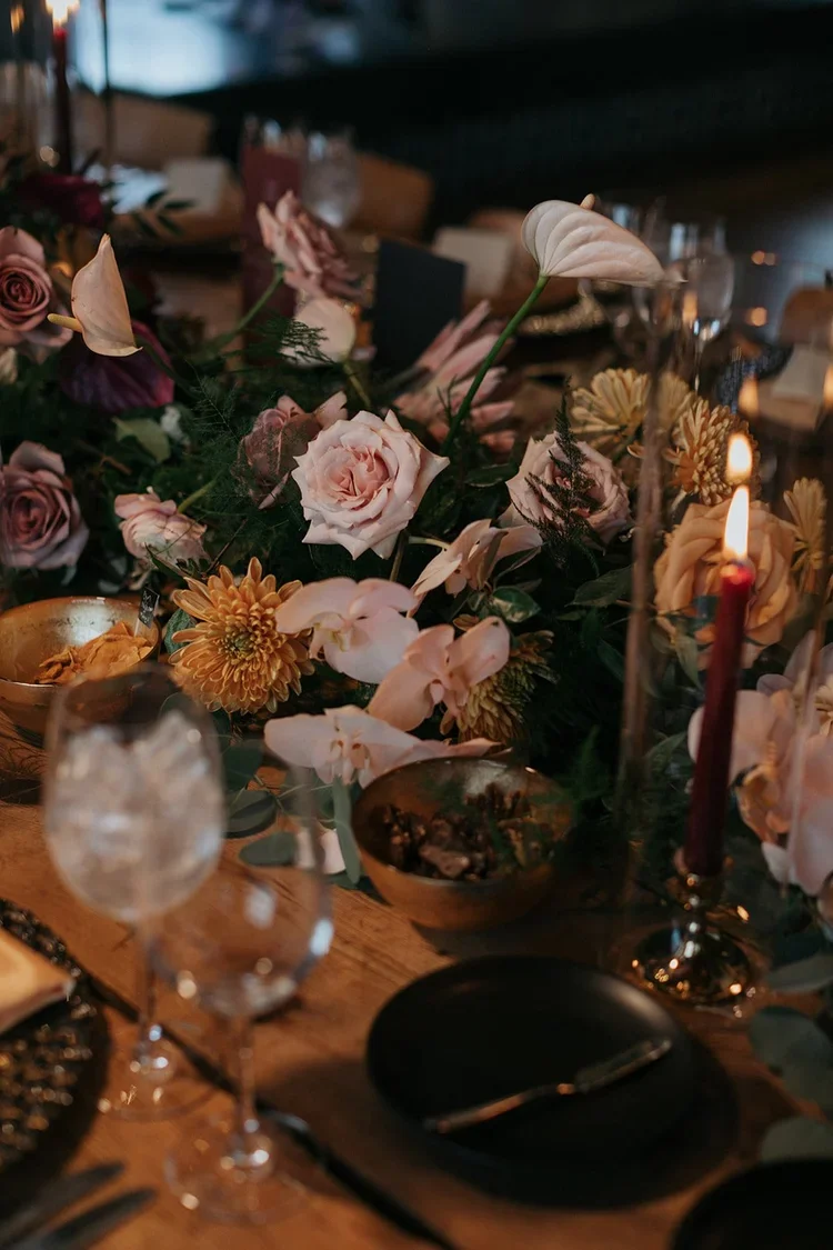 Elegant dinner table with a floral centerpiece, lit candle, wine glasses, and tableware.