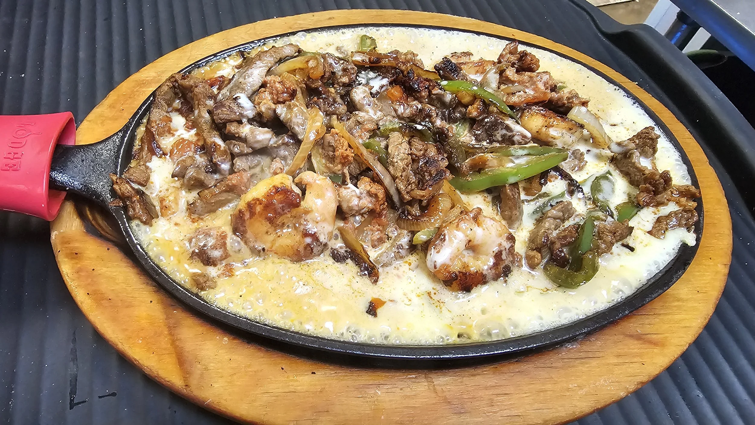 Sizzling plate of fajitas with sliced beef, shrimp, peppers, and onions on a wooden serving board.