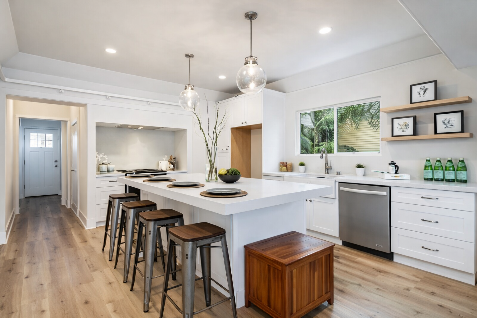 Modern kitchen with white cabinets, a large island with bar stools, and wooden accents. There are pendant lights above the island, a window over the sink, and minimalist decor.