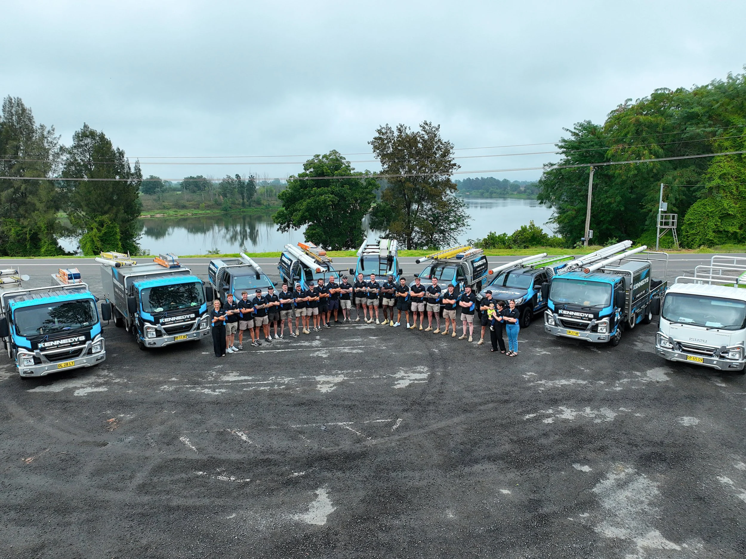 Team KPE standing in front of parked trucks with ladders, river and trees in the background.
