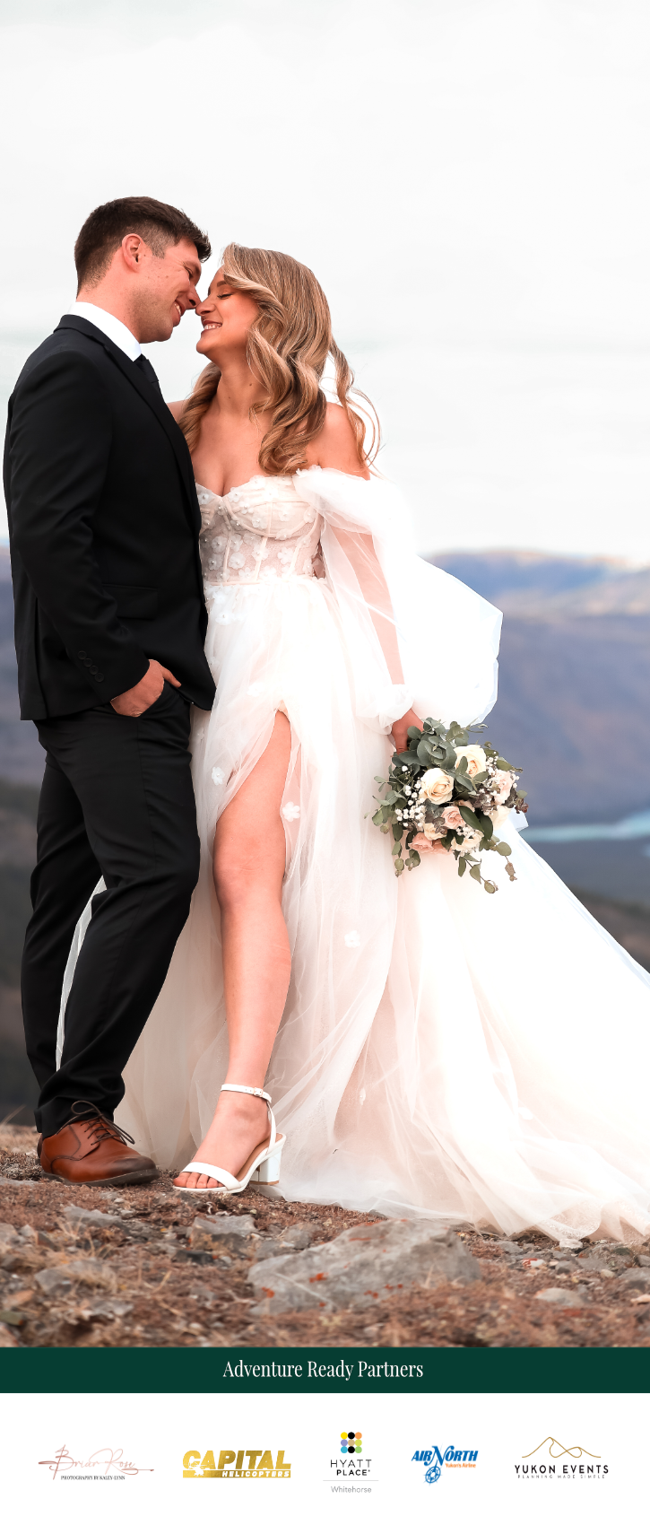 A bride and groom sharing a moment outdoors, dressed in wedding attire, with mountains and lake in the background.