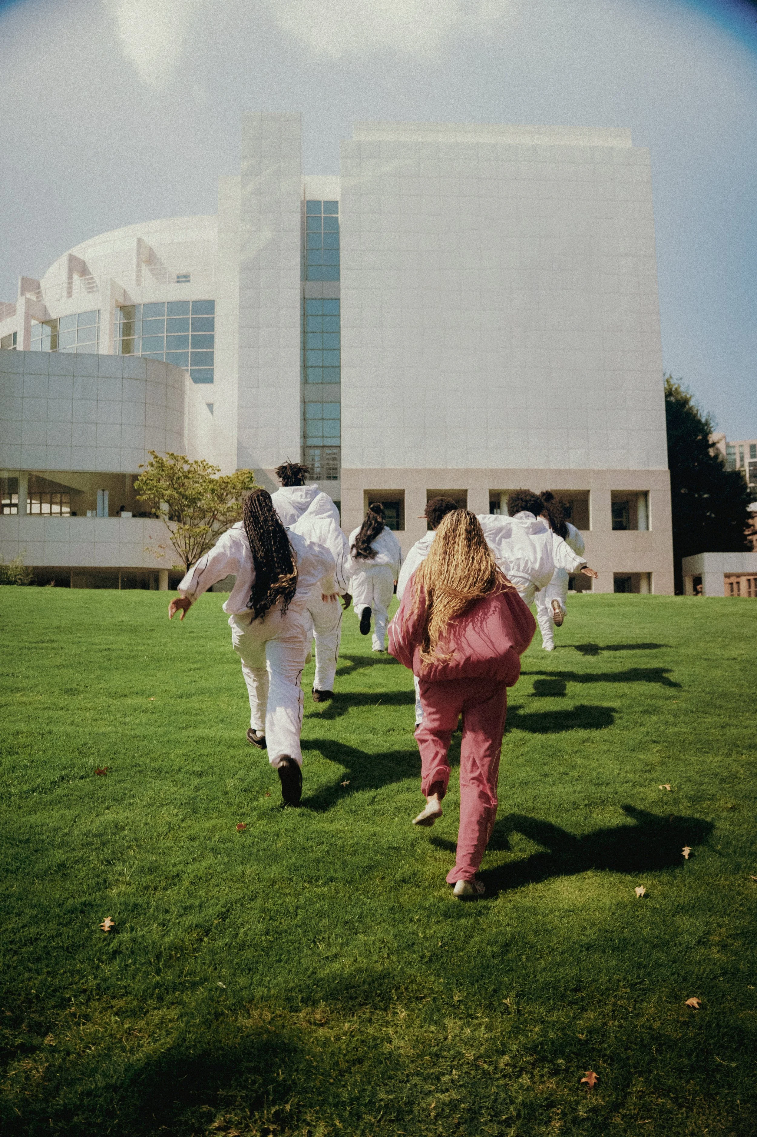 A group of people dressed in white and pink tracksuits running up a grassy hill towards a modern white building.
