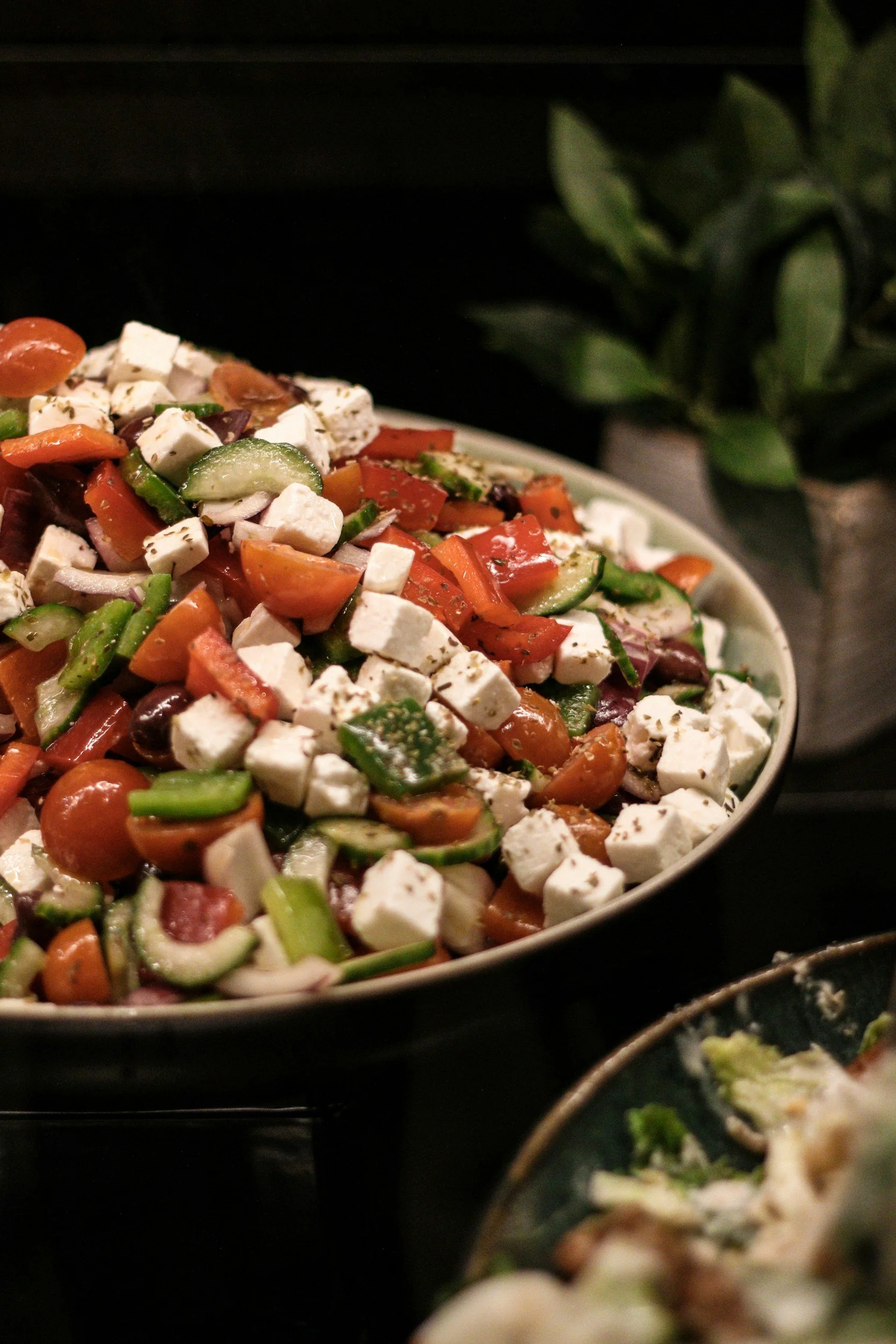 A salad with chopped tomatoes, cucumbers, red onions, black olives, feta cheese, and green herbs, served in a white bowl.