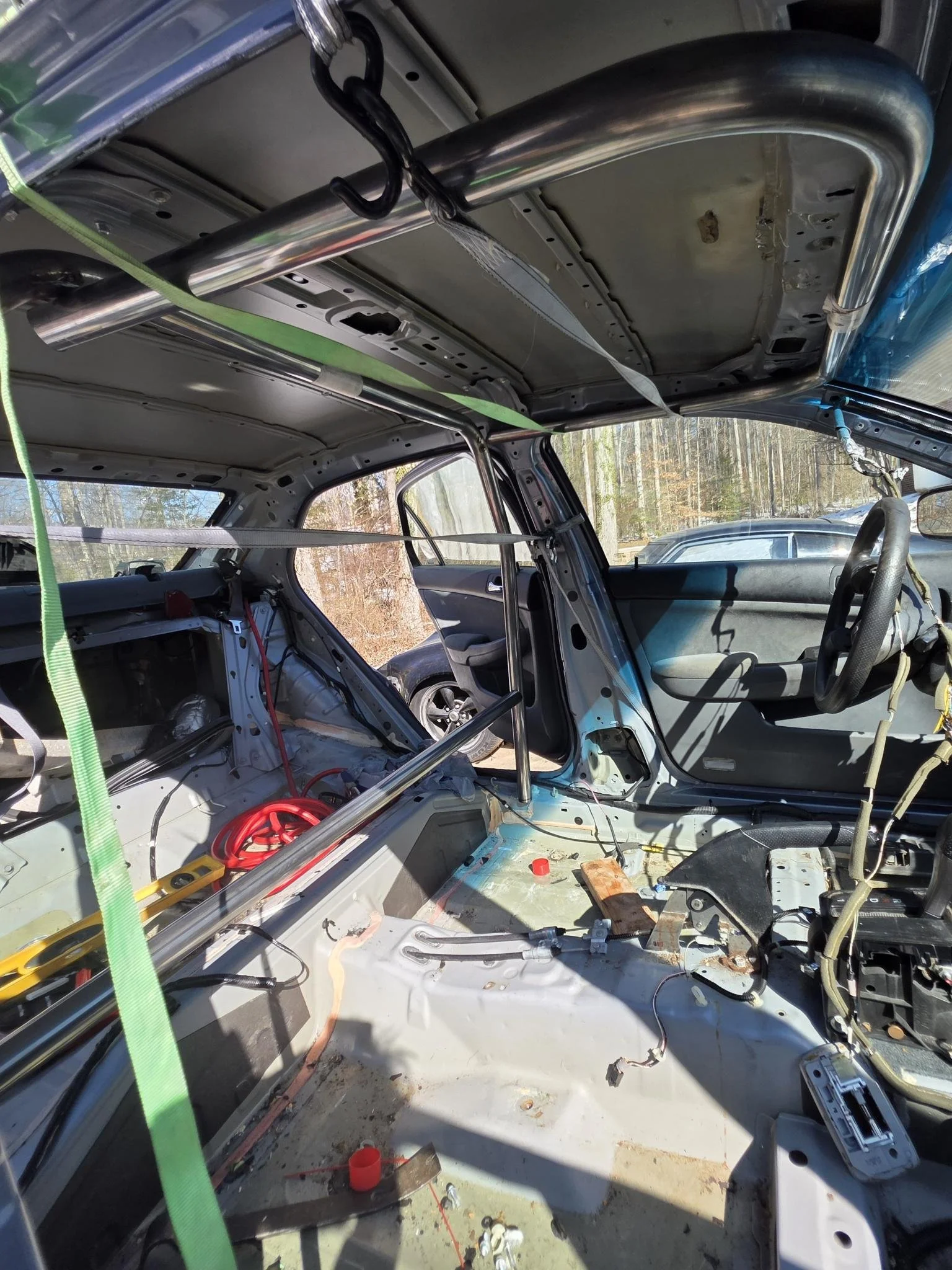 Interior of a car stripped for restoration or modification, showing exposed metal, wiring, and a roll cage, with some tools and components inside.
