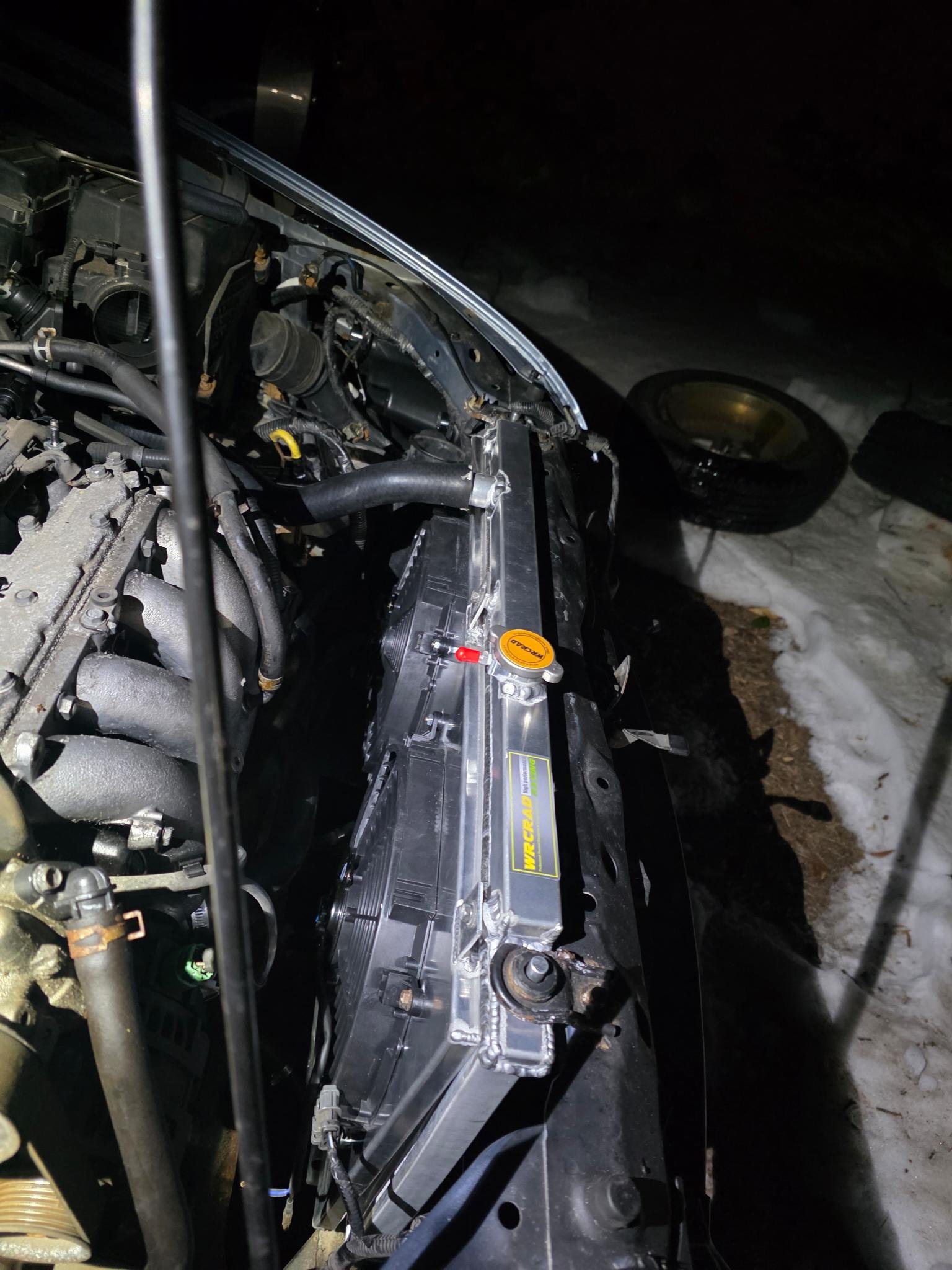 2007 Honda Accord engine with the hood open, located outdoors at night, with snow on the ground, and a detached tire in the background.