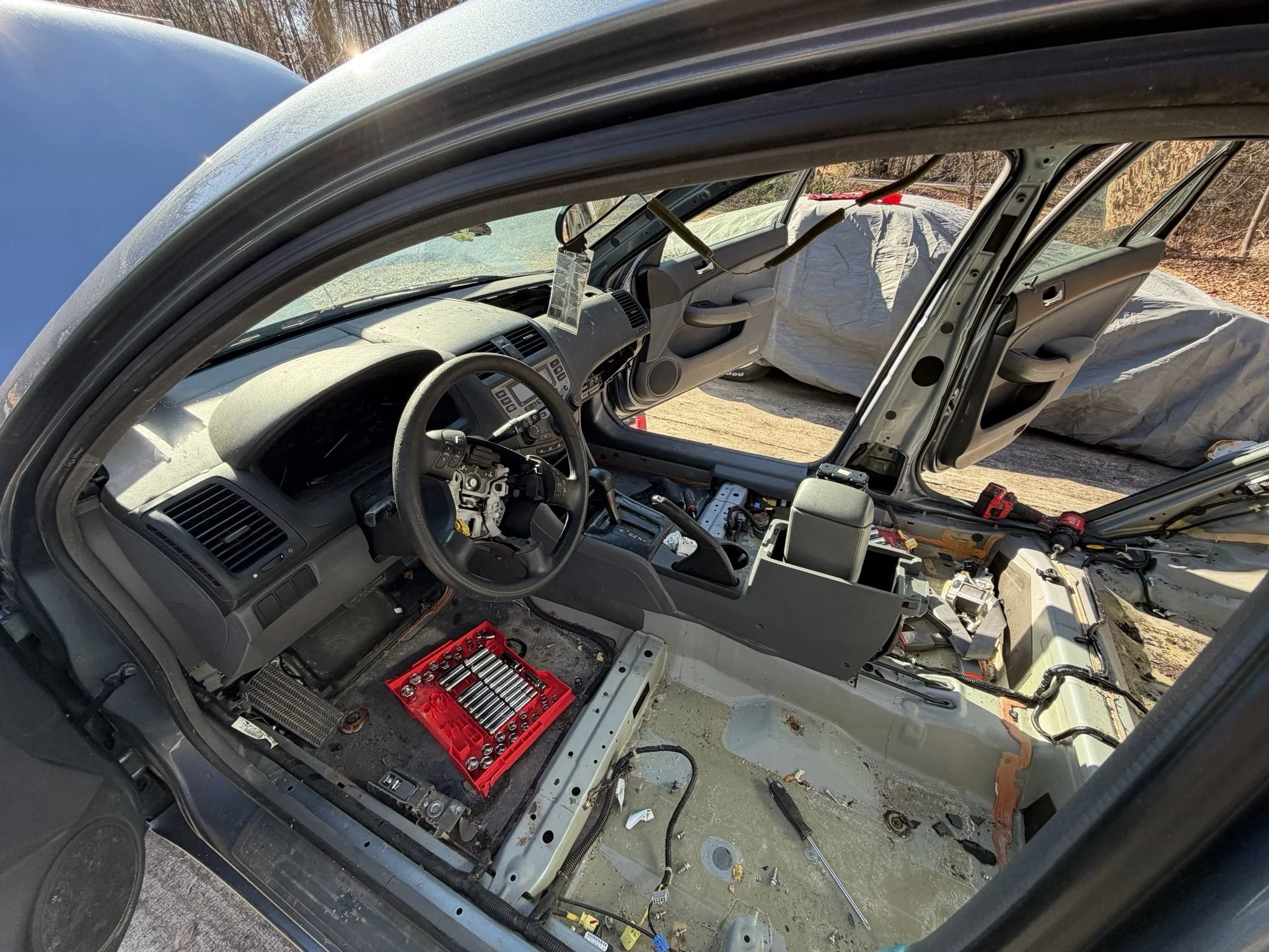 Inside of a car dashboard undergoing repairs, with tools and parts scattered around, including a red toolbox, disassembled panels, and missing seats.