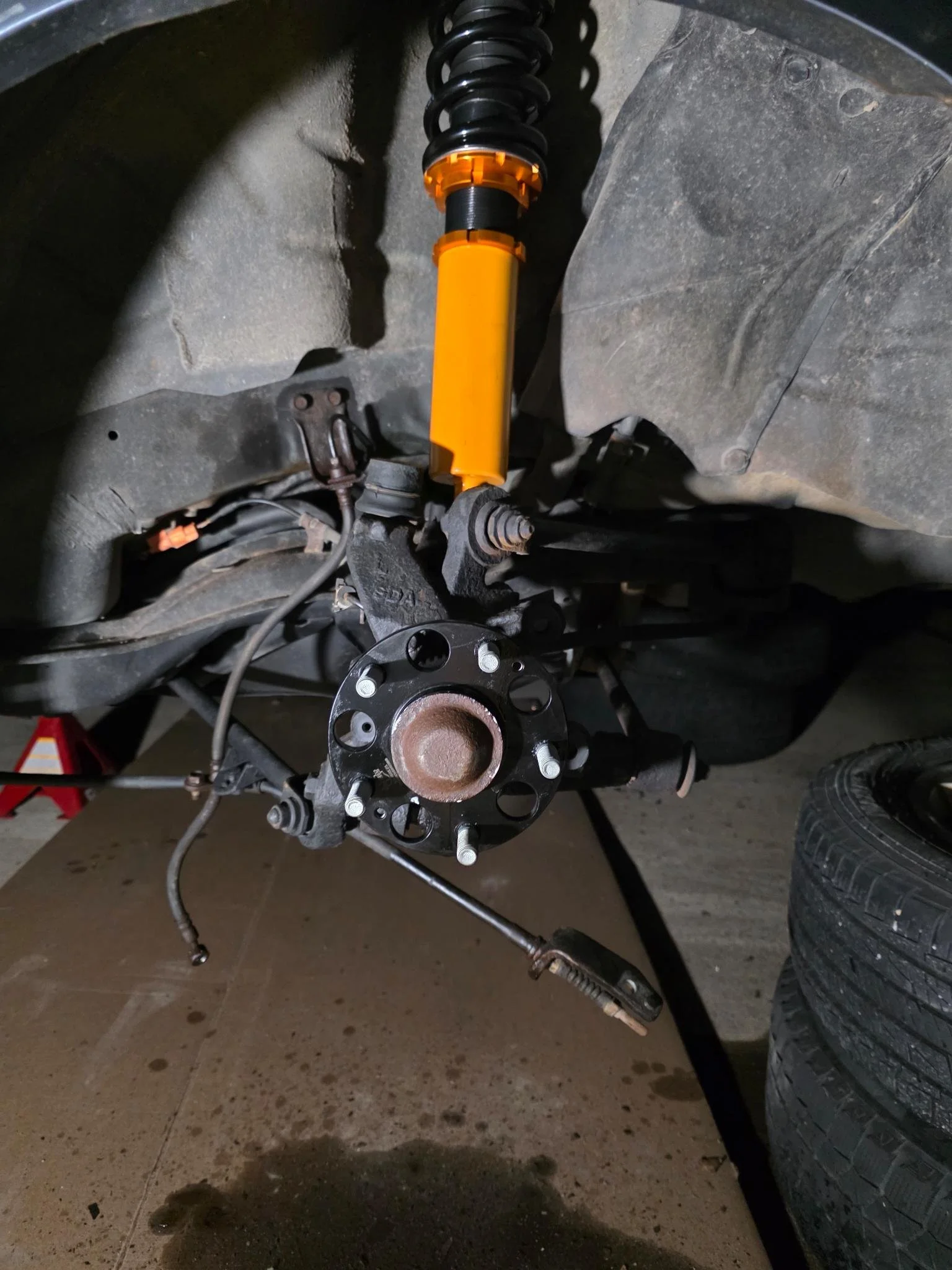 A 2007 Honda Accord front suspension and wheel hub assembly are being repaired, with the wheel removed, revealing the brake rotor and hub, and a new yellow shock absorber installed.