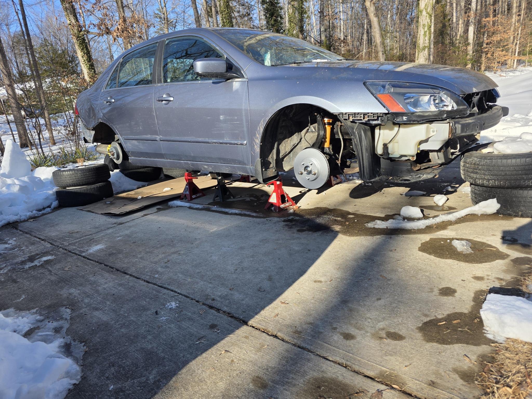 A 2007 Honda Accord is elevated on red jack stands, undergoing extensive repairs and modifications in preparation for endurance racing.  Front bumper and grille are removed to provide access to engine bay