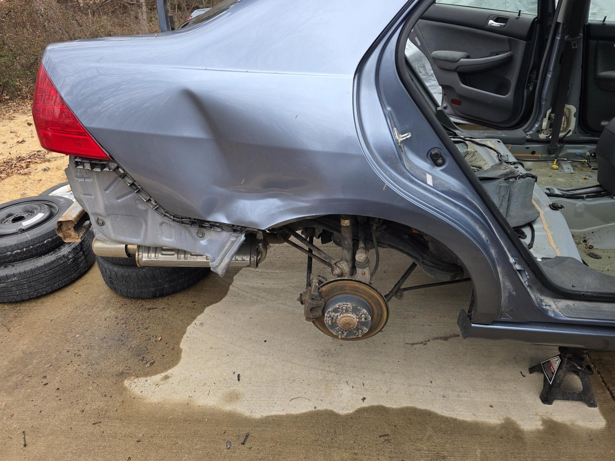 Gray car with rear wheel and parts removed, inside view of the interior, car on jack stands, vehicle appears to be undergoing repair or restoration.