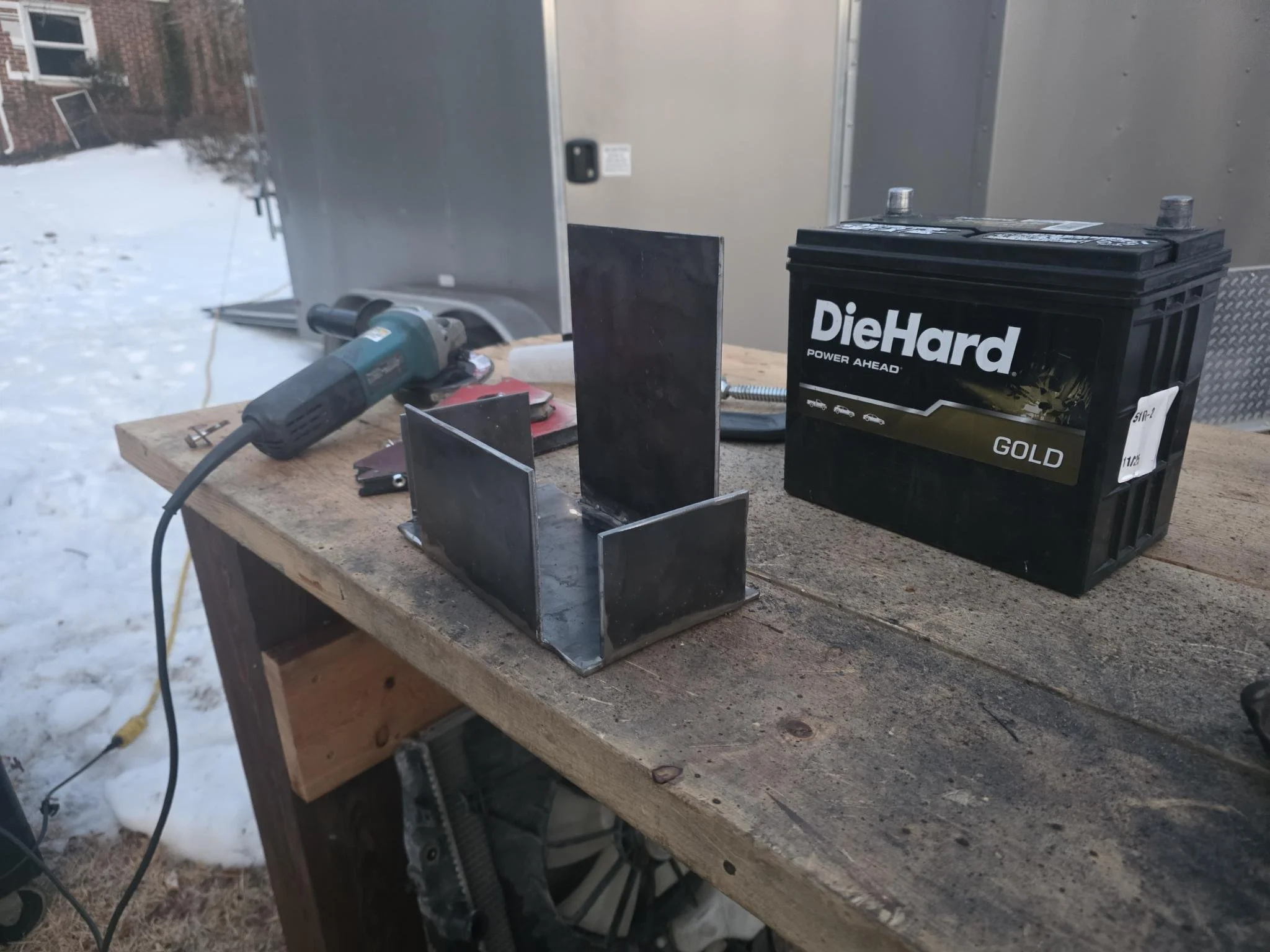 A workbench outdoors with a power drill, a partially assembled metal structure, and a black DieHard GOLD car battery. custom battery box for 2007 Honda Accord