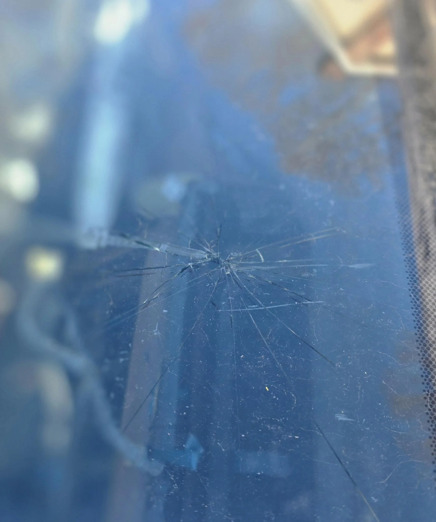 Close-up of a cracked windshield with multiple spiderweb cracks on a blue surface.