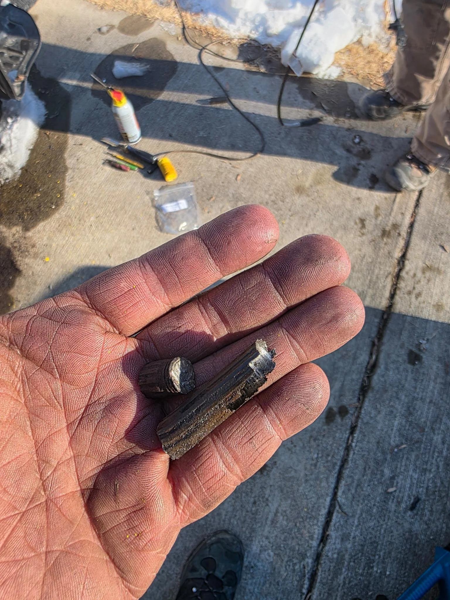 Close-up of a person's dirty hand holding the shaft of a broken lower strut mount bolt for a 2007 Honda Accord.