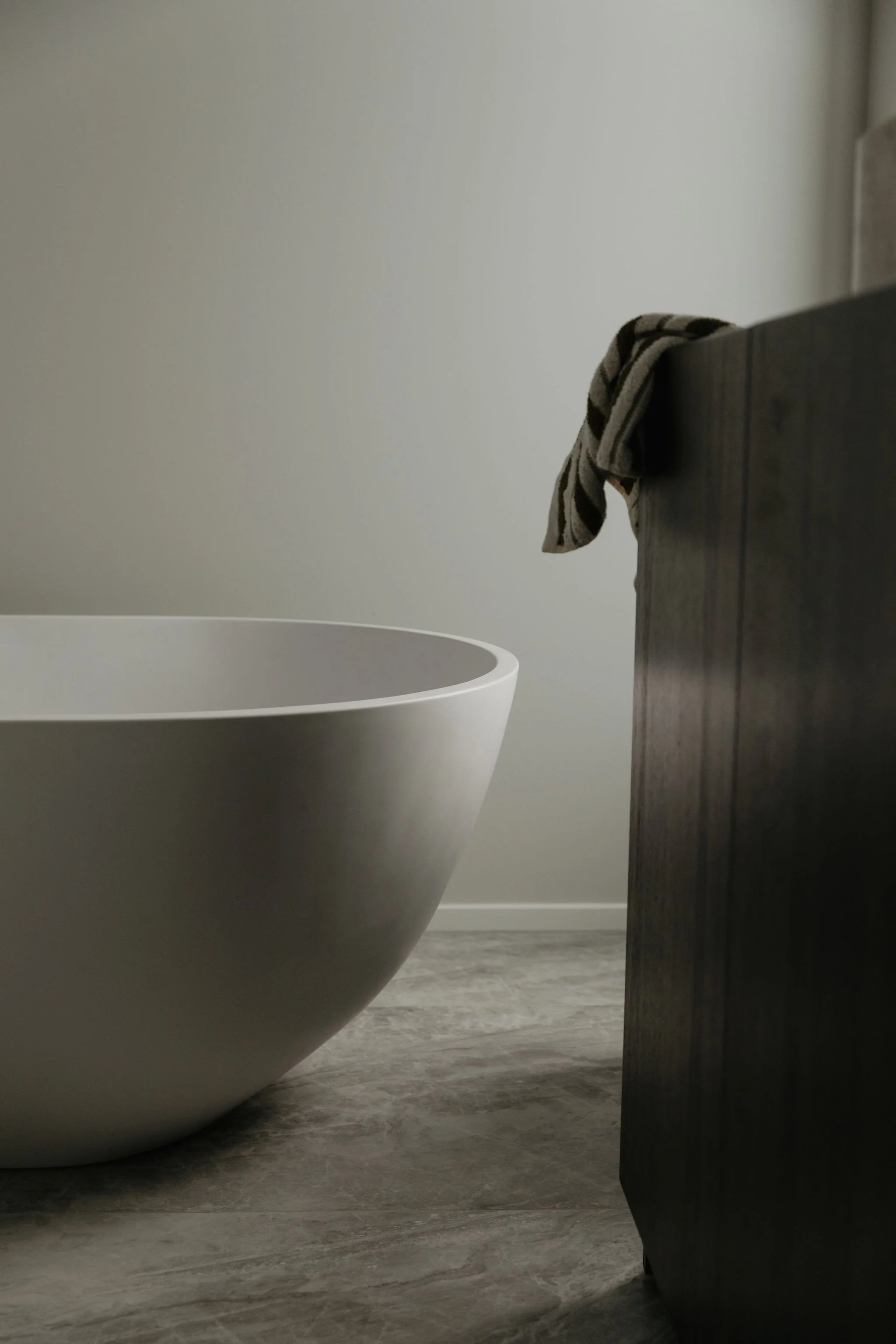 Minimalist bathroom scene with a modern white bathtub and a dark wooden cabinet, with a striped towel draped over the cabinet.