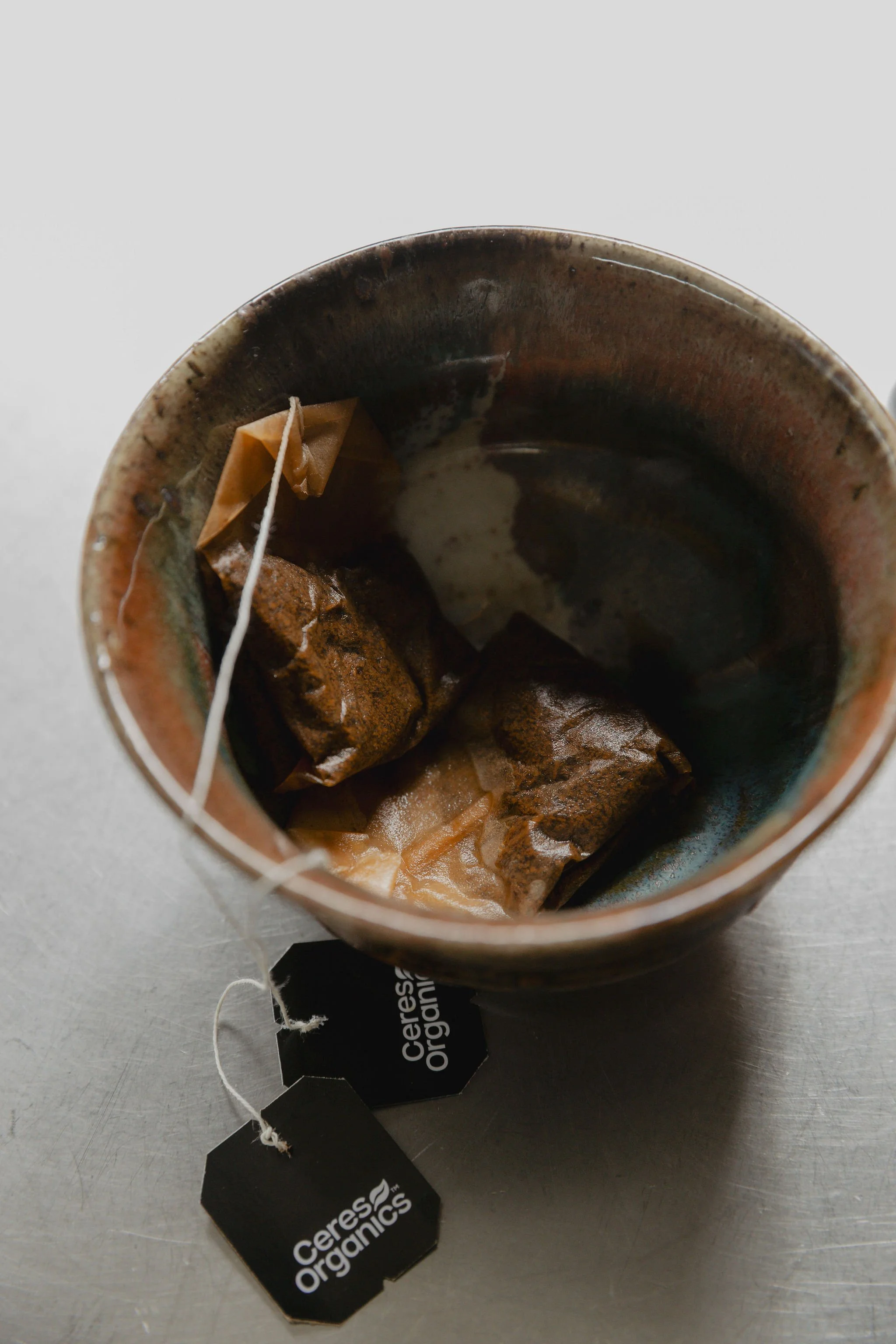 A ceramic mug holds used tea bags, next to a black tag with white text reading 'Ceres Organics'.