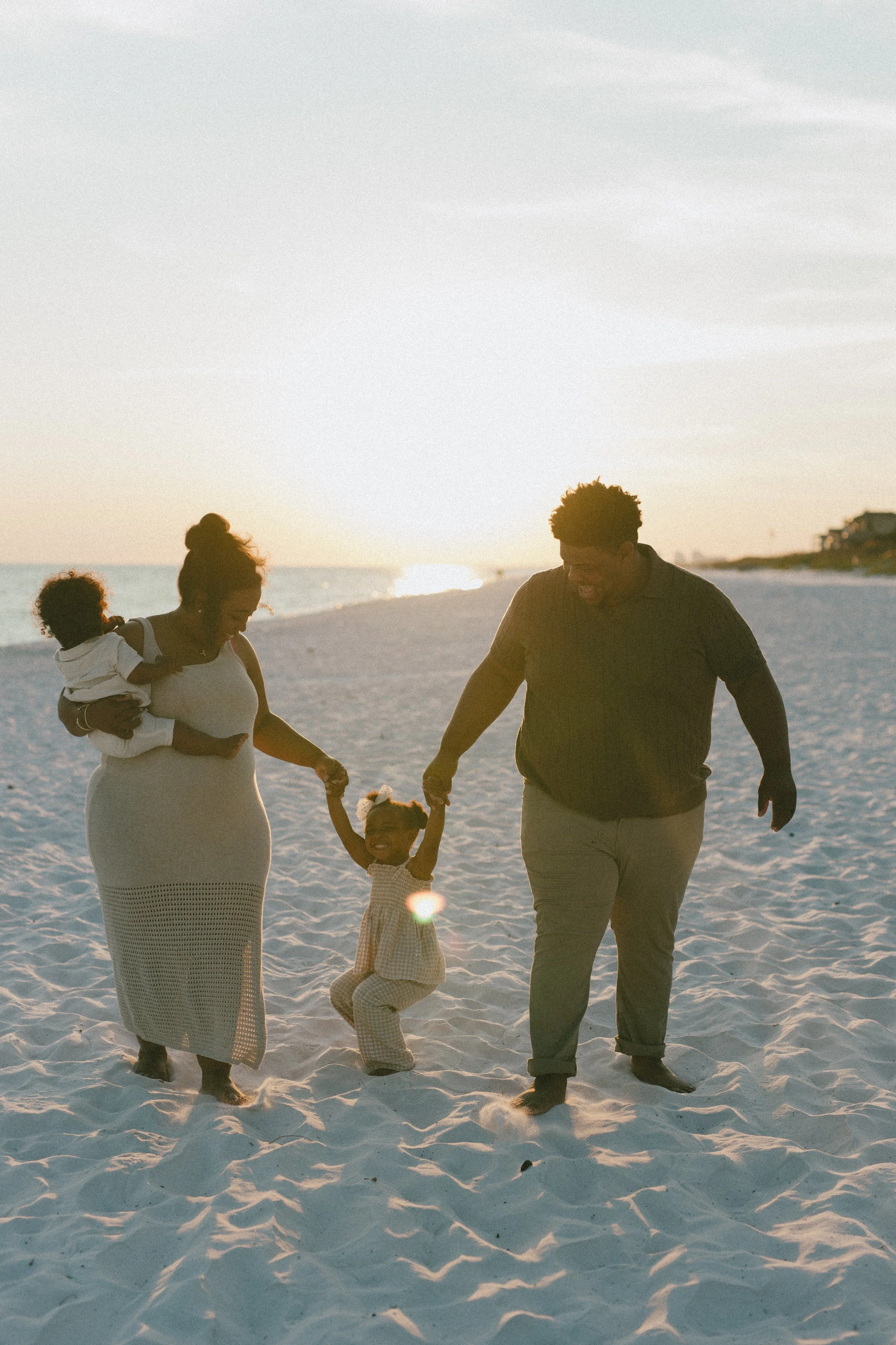 Family holding hands and playing on the beach at sunset.